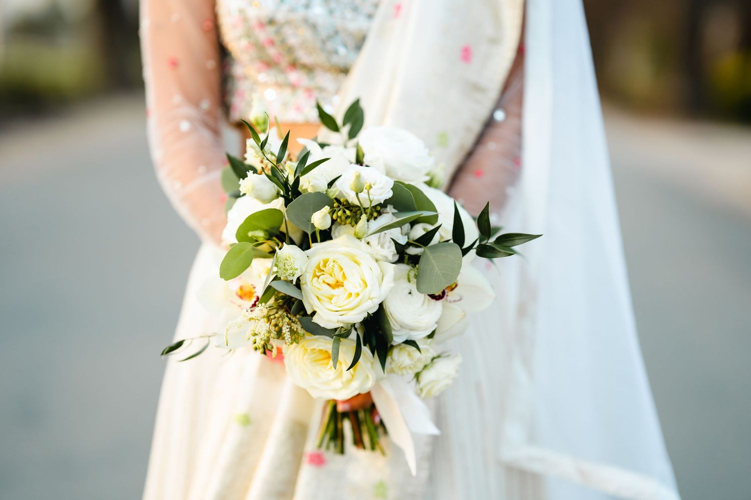 An elegant white and cream wedding bouquet with roses and greenery against a lace dress.