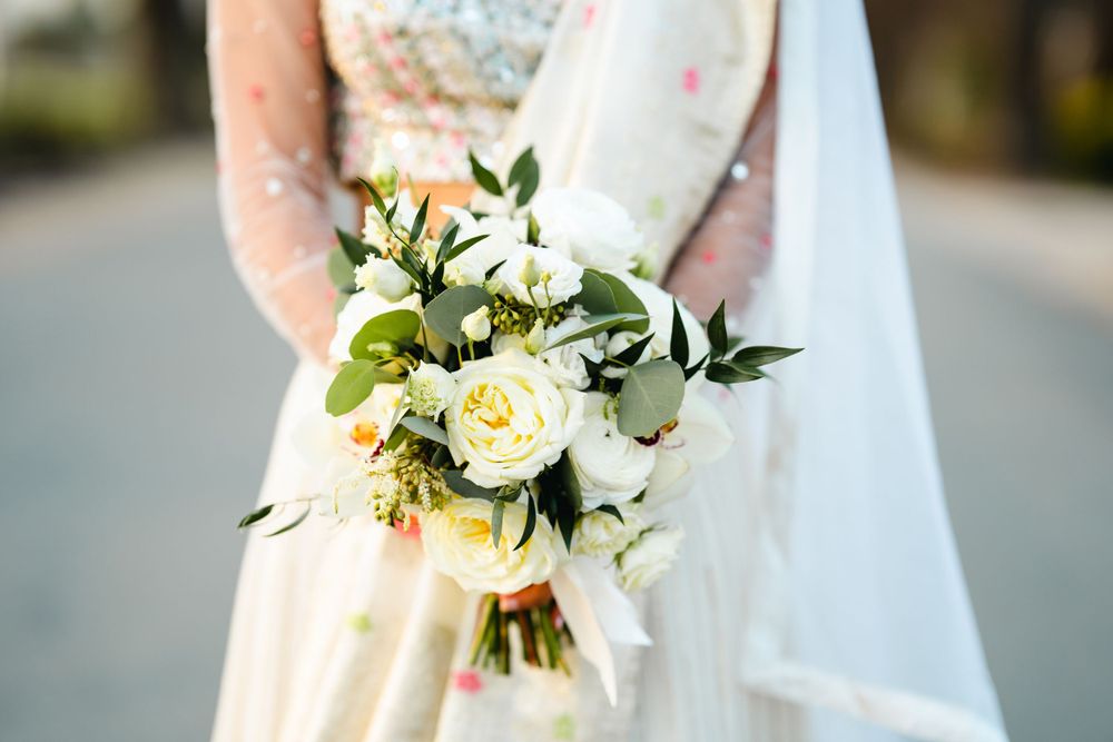 An elegant white and cream wedding bouquet with roses and greenery against a lace dress.