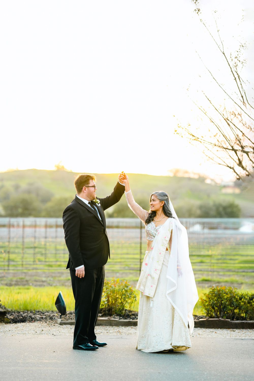 A joyful wedding couple high-fiving during their sunset photo session near a vineyard.