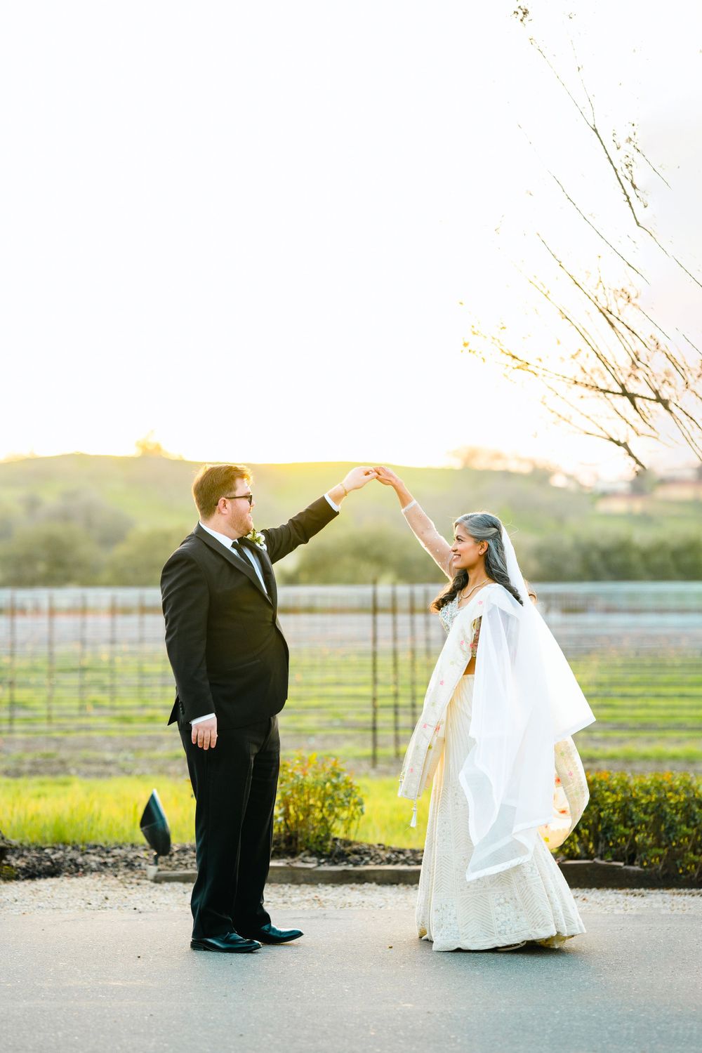 A couple shares a playful dance move during their wedding portraits at sunset.