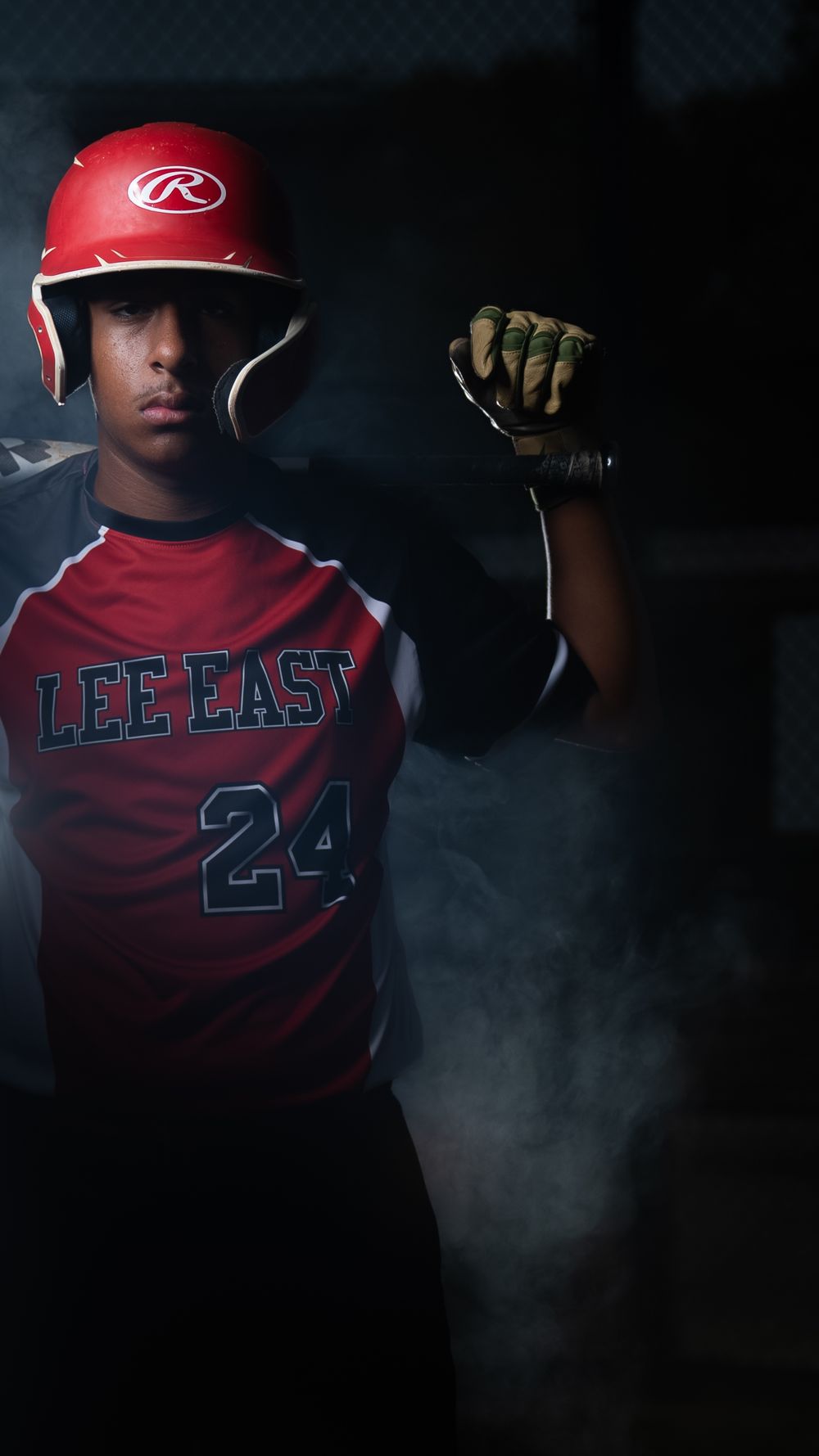 Baseball player in red Lee East jersey number 24 stands in dramatic lighting with batting helmet and glove.