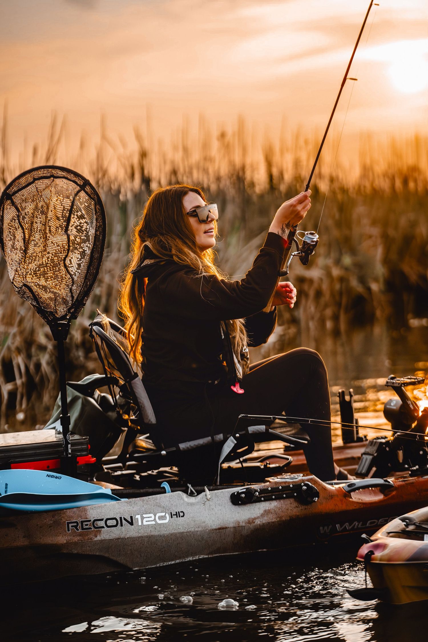 Kayak fishing scene at golden hour with fishing rod and net.
