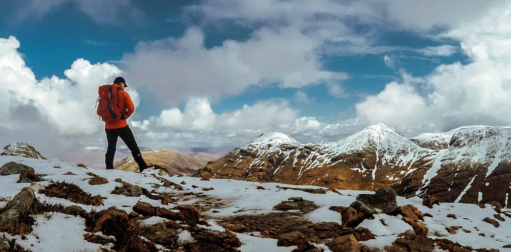 A panoramic mountain landscape with snow-capped peaks and dramatic clouds stretching across the horizon.