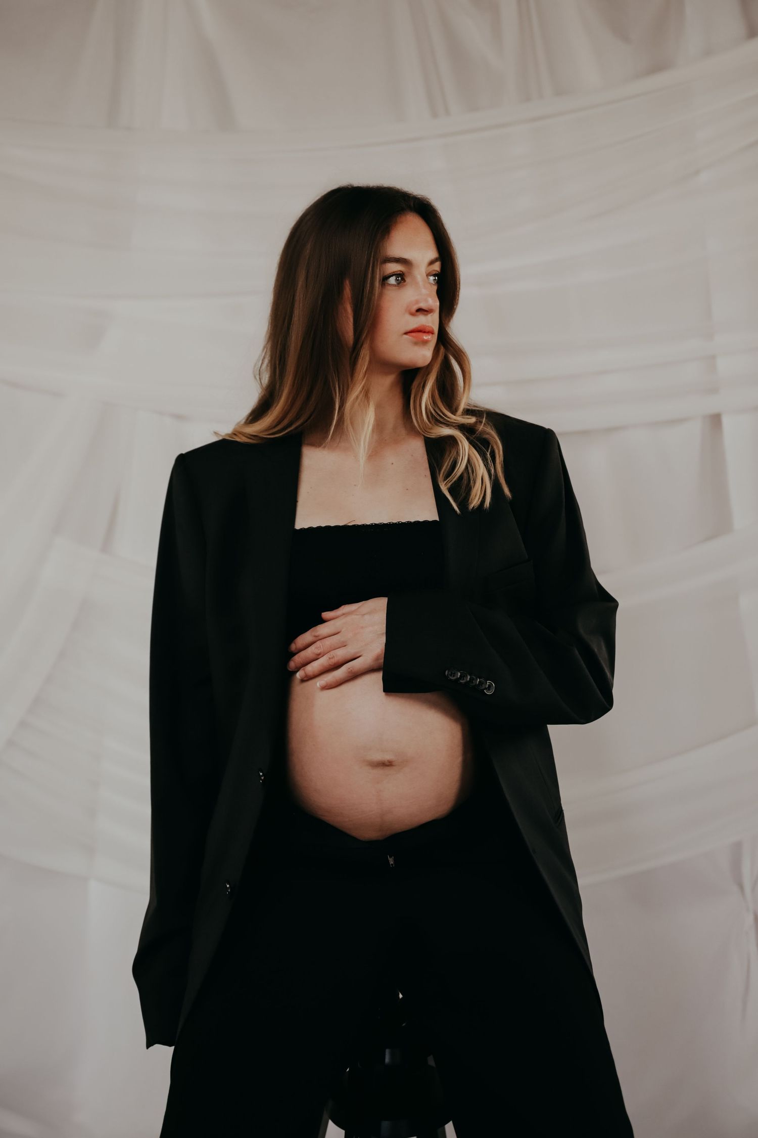 A maternity portrait featuring a woman in a black blazer against a white backdrop.
