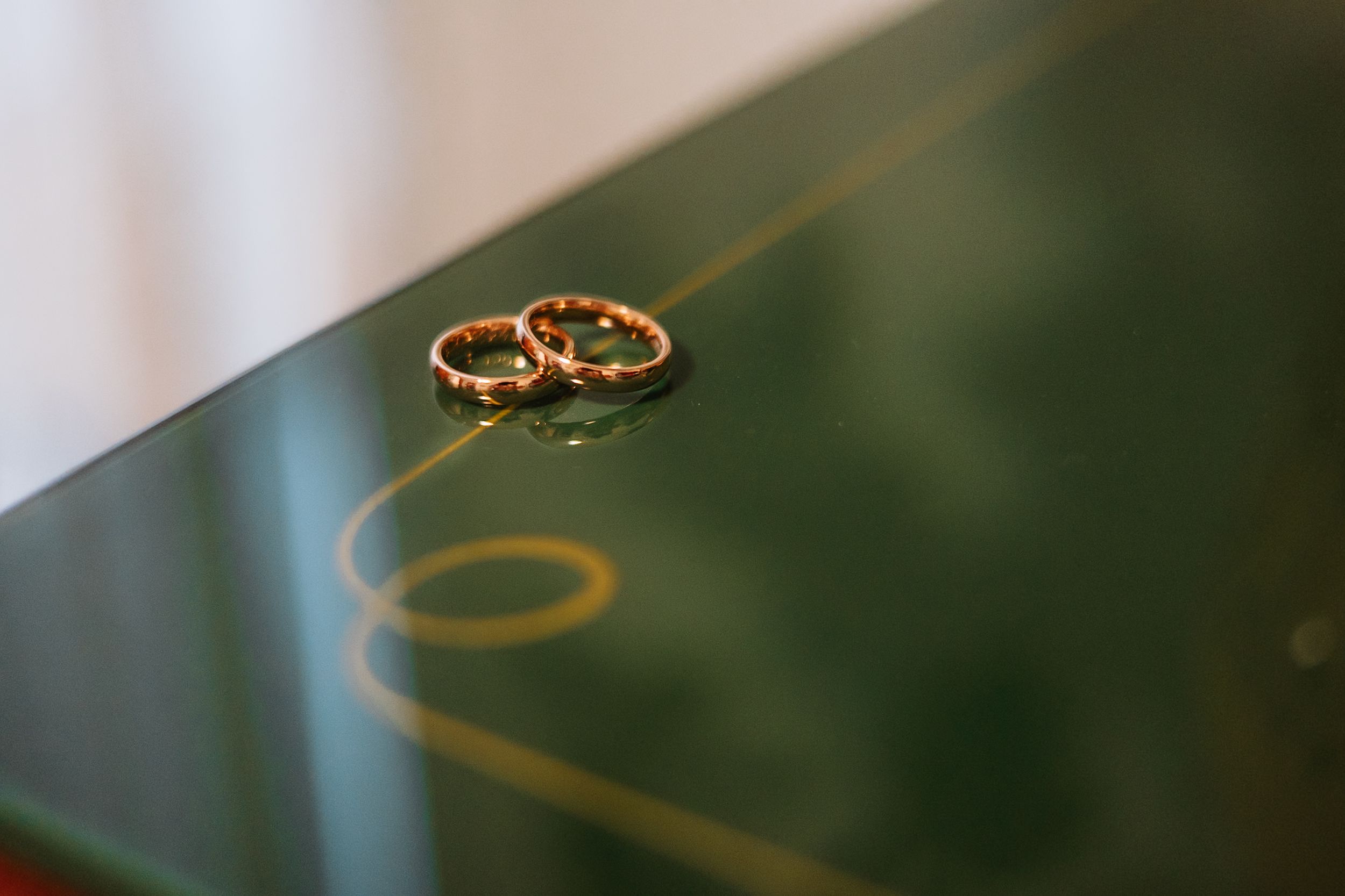 Two gold wedding rings sit on a reflective dark surface casting a soft shadow.