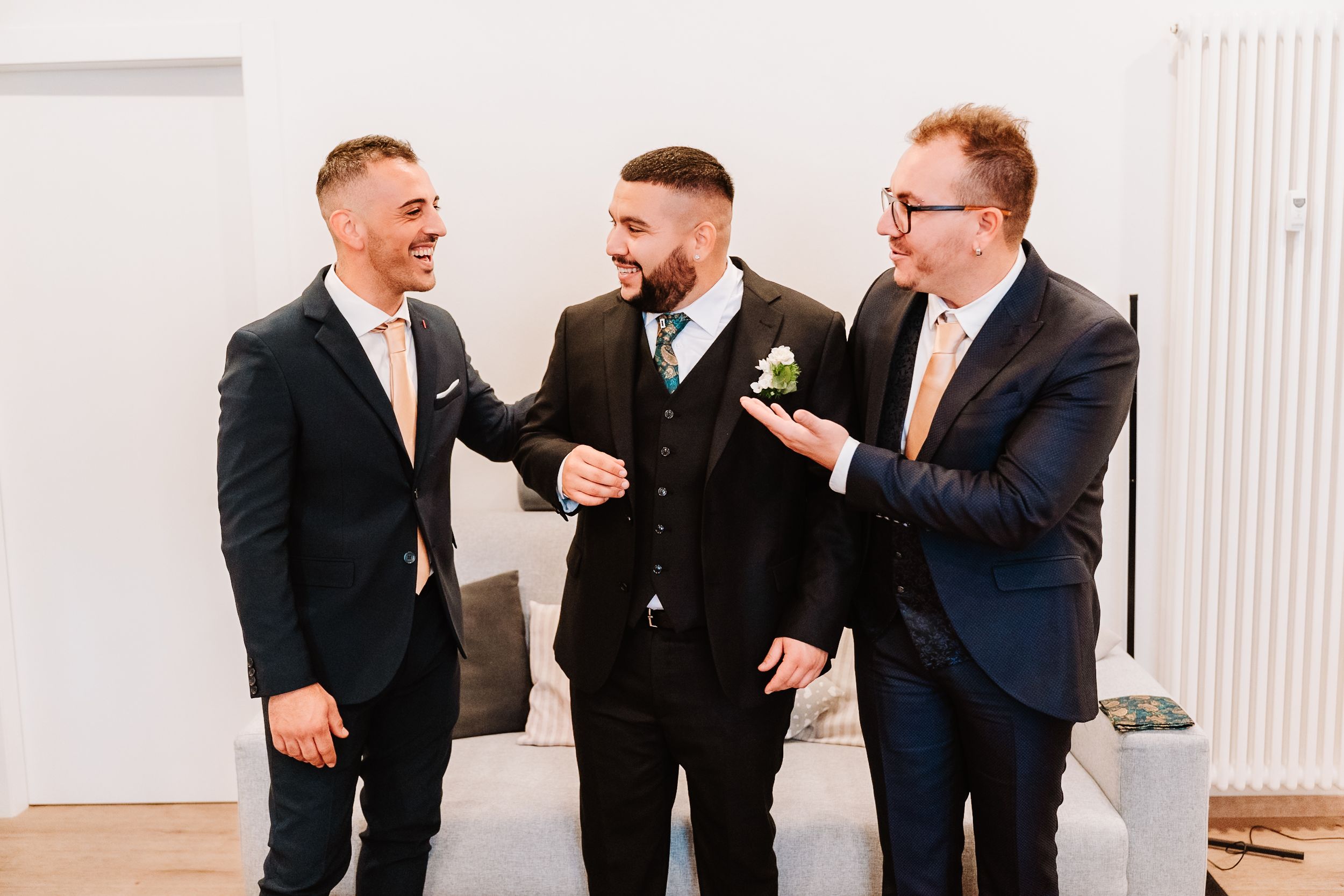 Three well-dressed men in suits share a lighthearted moment together at a formal event.