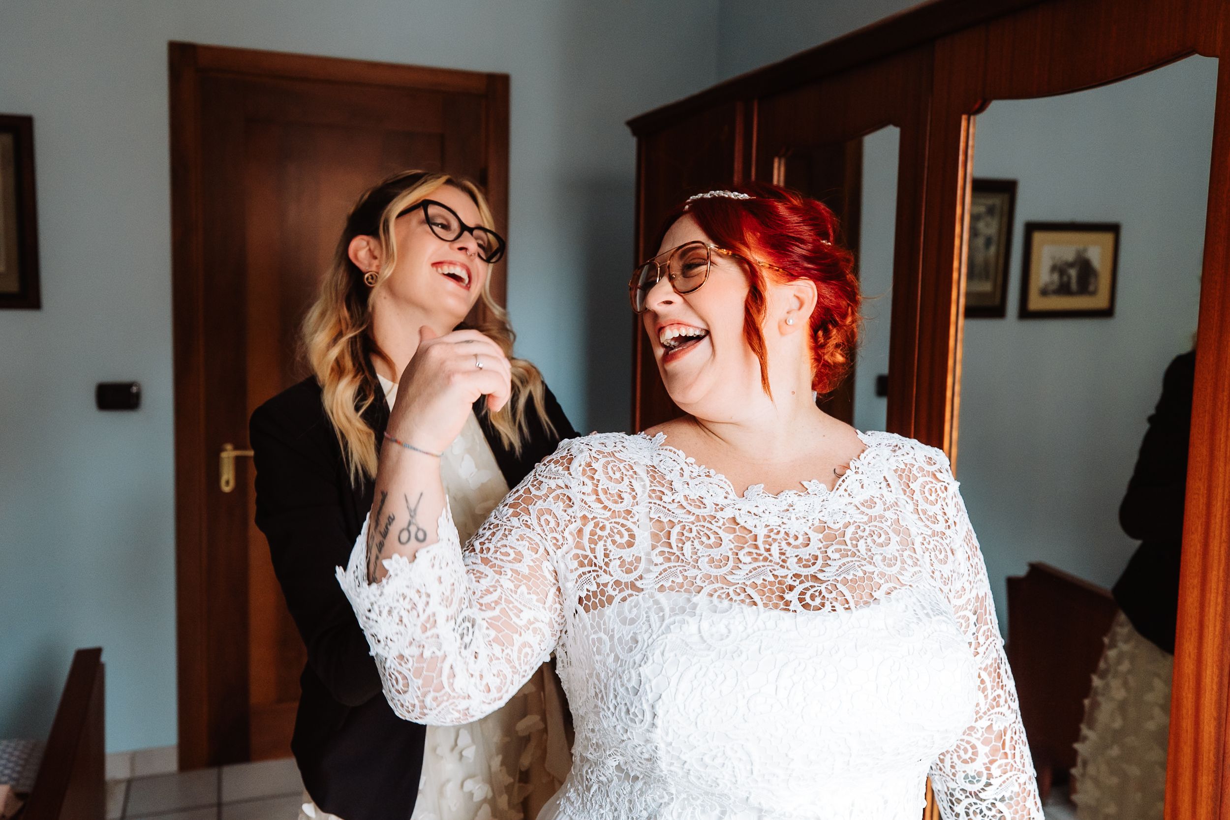 Two people share a joyful moment together while laughing, with one wearing a delicate white lace gown.