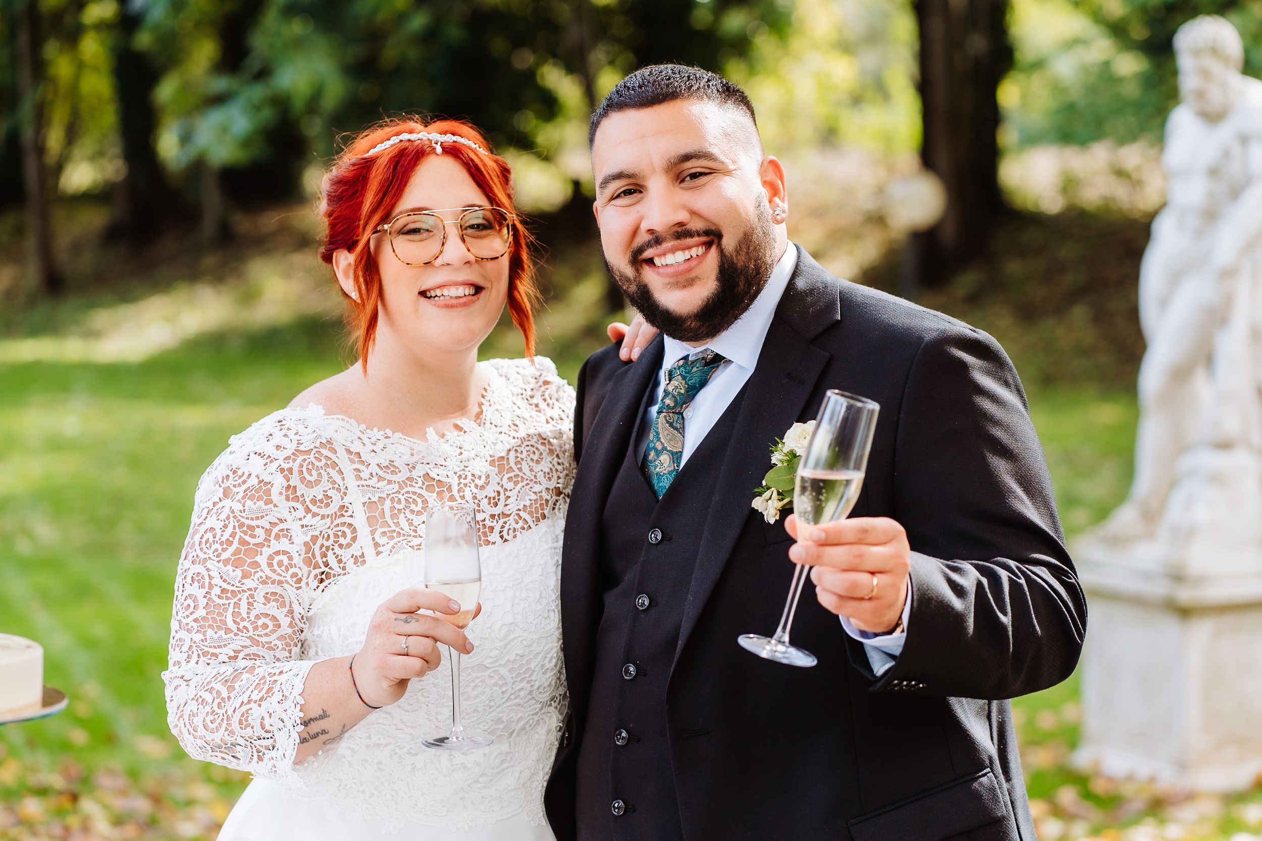 A joyful newlywed couple toast with champagne glasses in an outdoor garden setting.