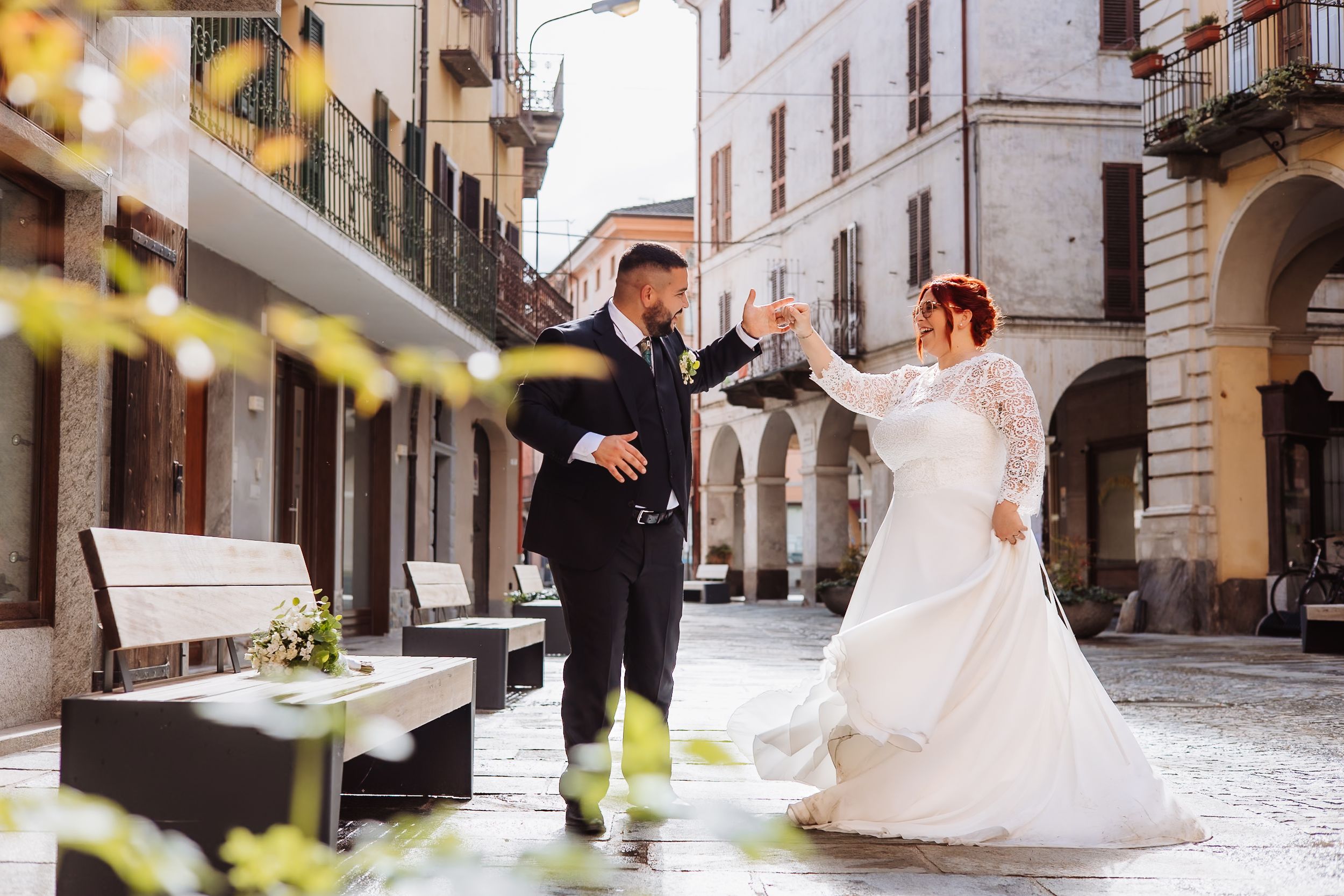 A joyful dance between two people in formal attire on a quaint European cobblestone street.