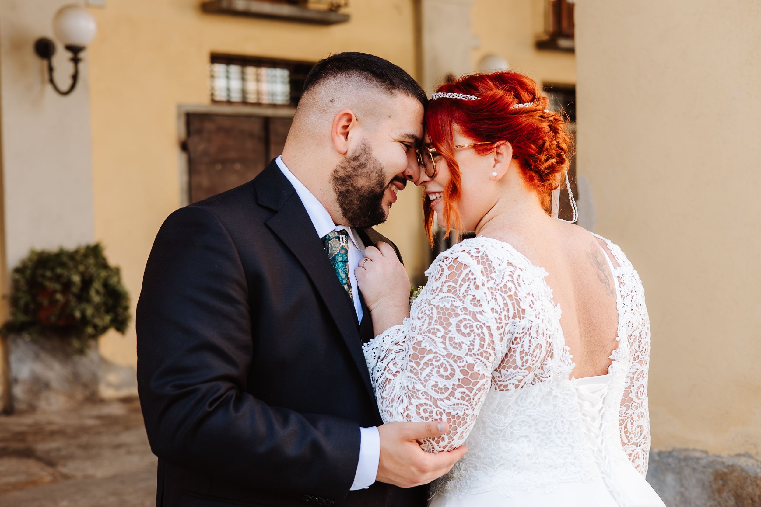 Newlyweds share an intimate moment in front of a building, bride wearing lace dress with open back detail.