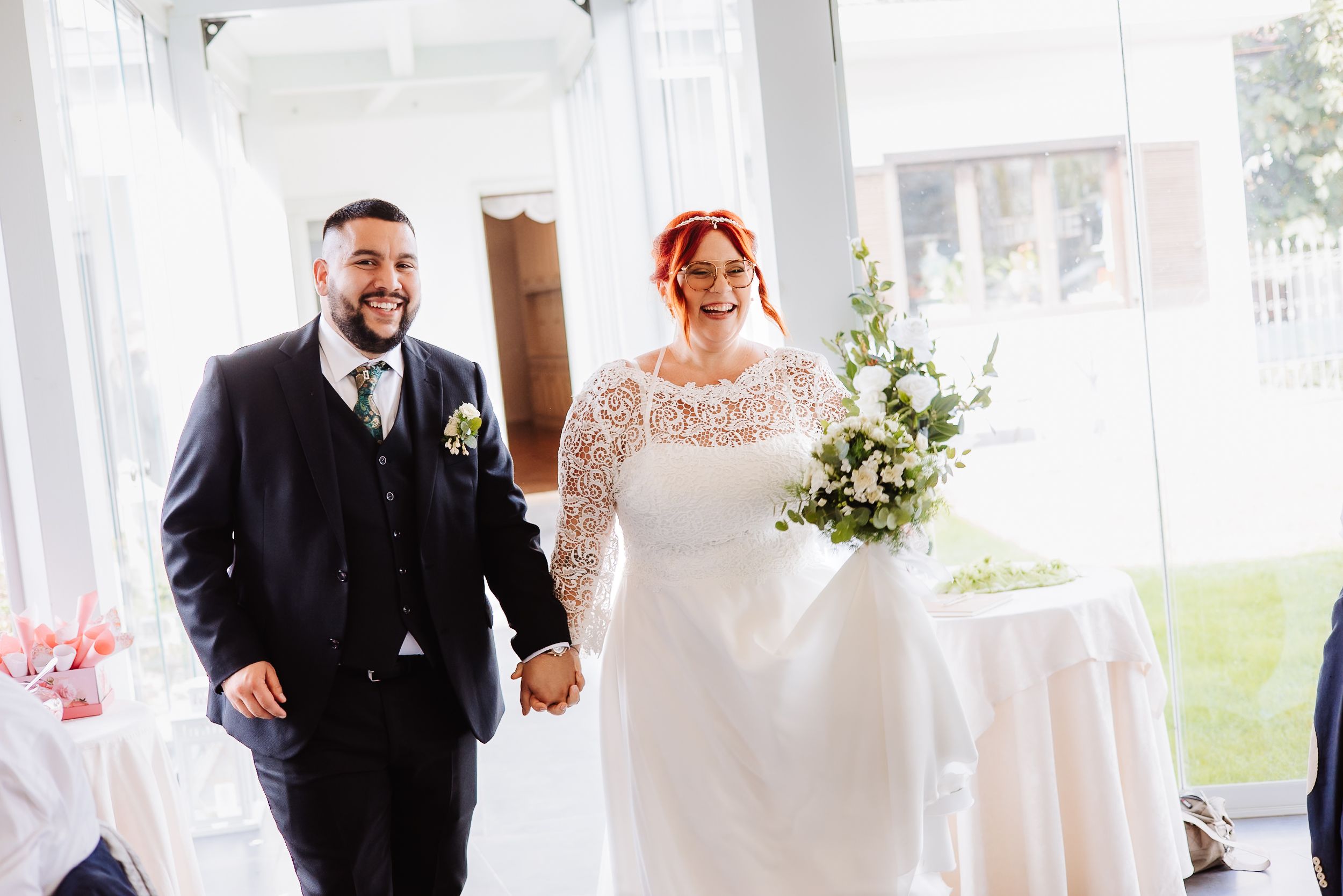 A couple smiles joyfully while walking hand in hand at their wedding reception under a white tent.