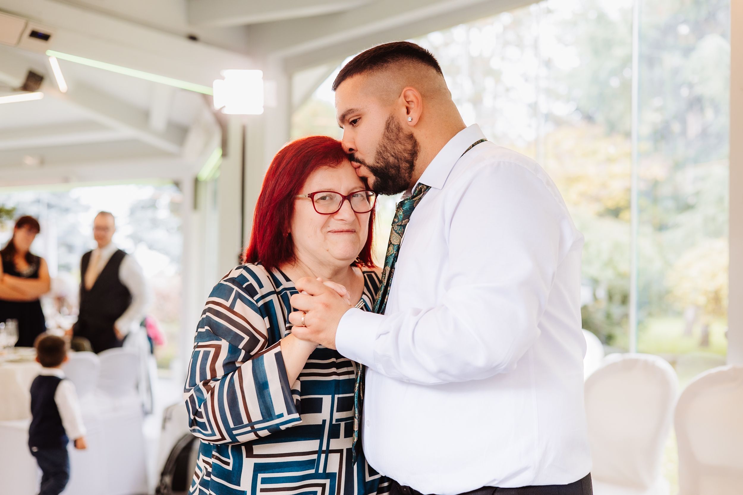 A couple shares an intimate moment while dancing together at an indoor venue with windows and white decor.