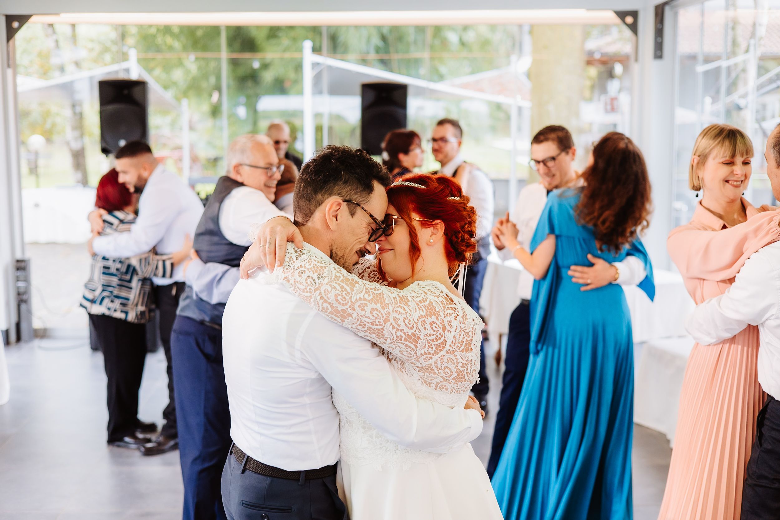 Couples dance together in a bright sunlit venue, with a woman in a blue dress and others in formal attire visible.