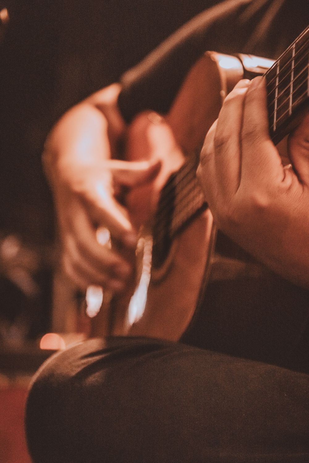 Close-up shot of hands playing acoustic guitar strings in warm ambient lighting.