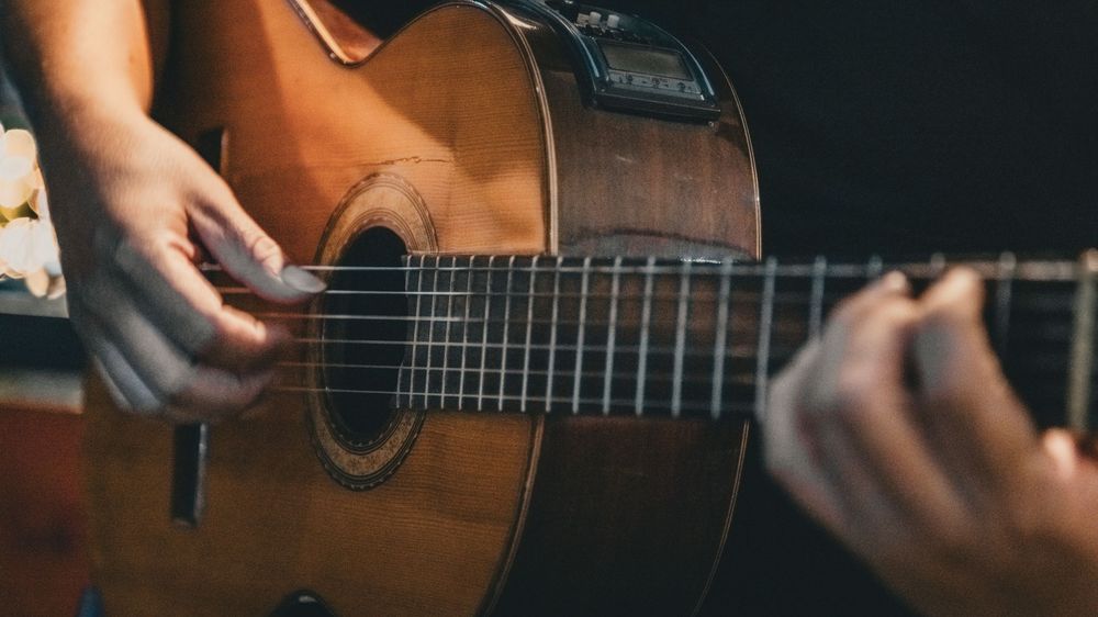 Hands strumming acoustic guitar strings in warm lighting.
