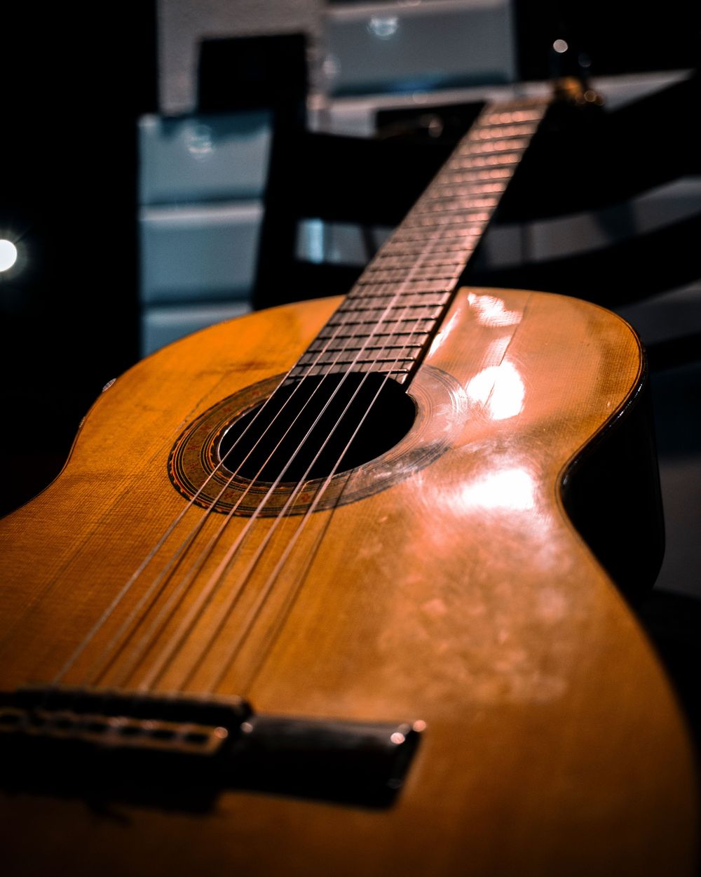 Close-up of a honey-colored acoustic guitar body and fretboard in dramatic lighting.