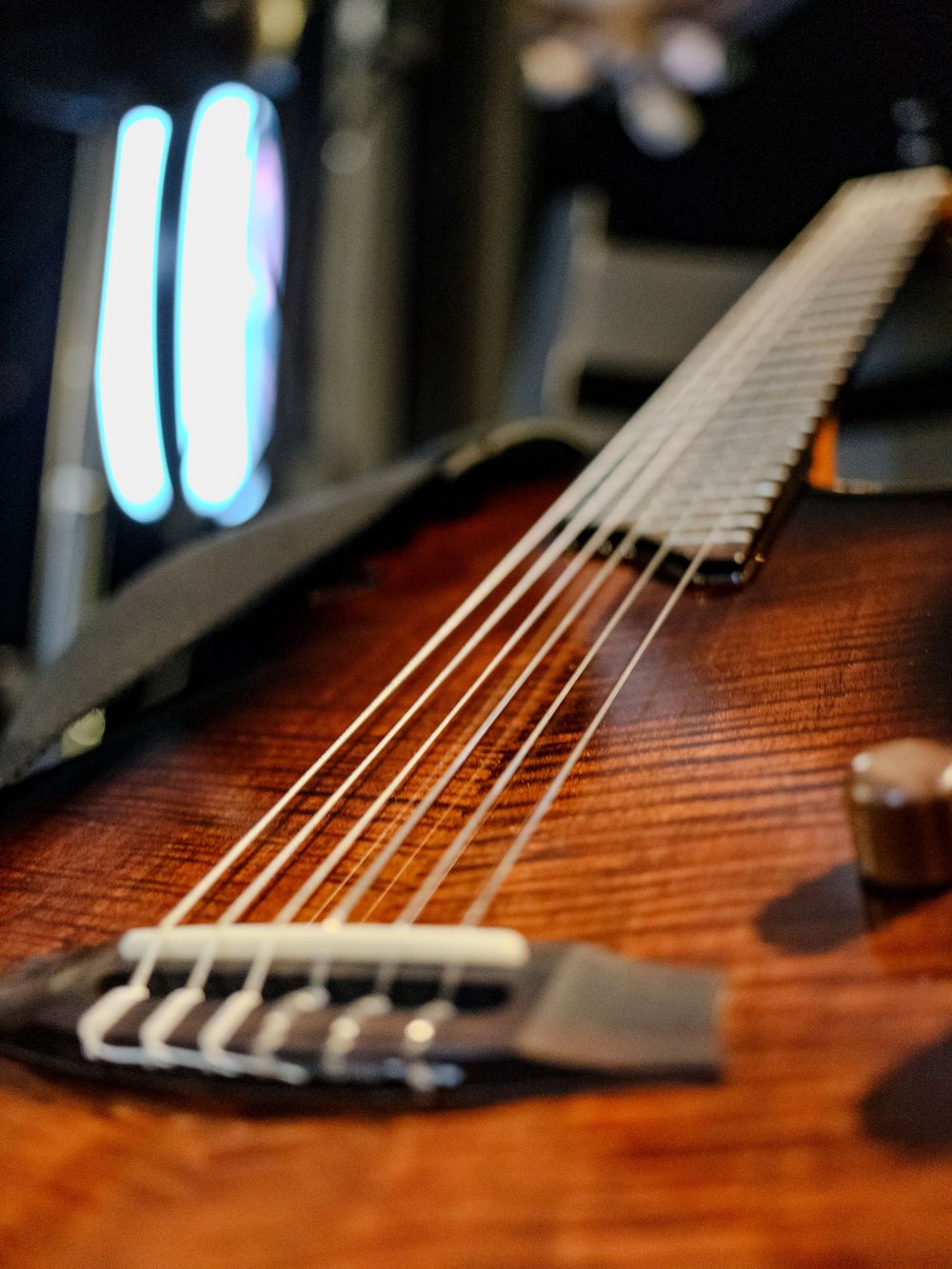 Detail shot of wooden guitar bridge and strings with blue lights in background.