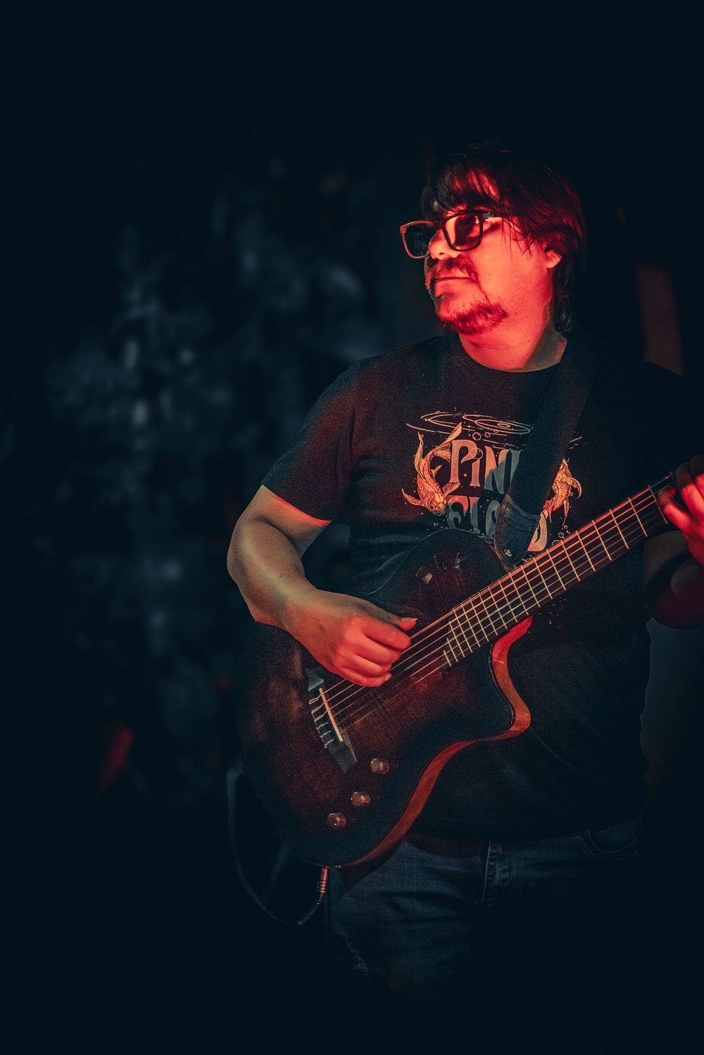 Musician plays electric guitar under red stage lighting during live performance.