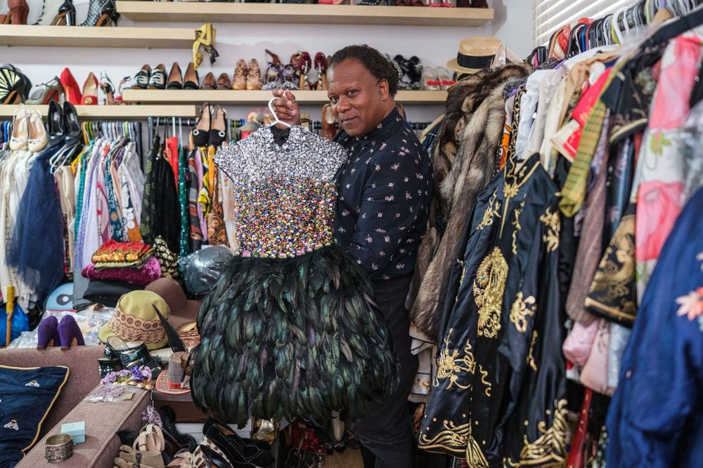 Person examines a sequined garment while browsing through a colorful vintage clothing rack in a thrift store.