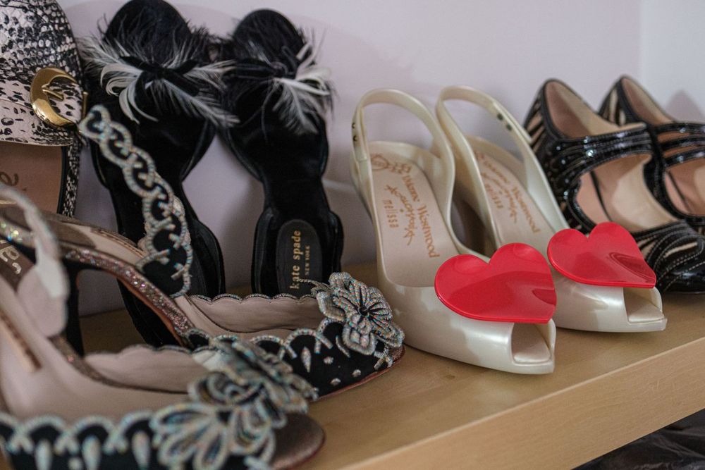 Stylish women's shoes including black patterned heels and white sandals with red bows arranged on a shelf.