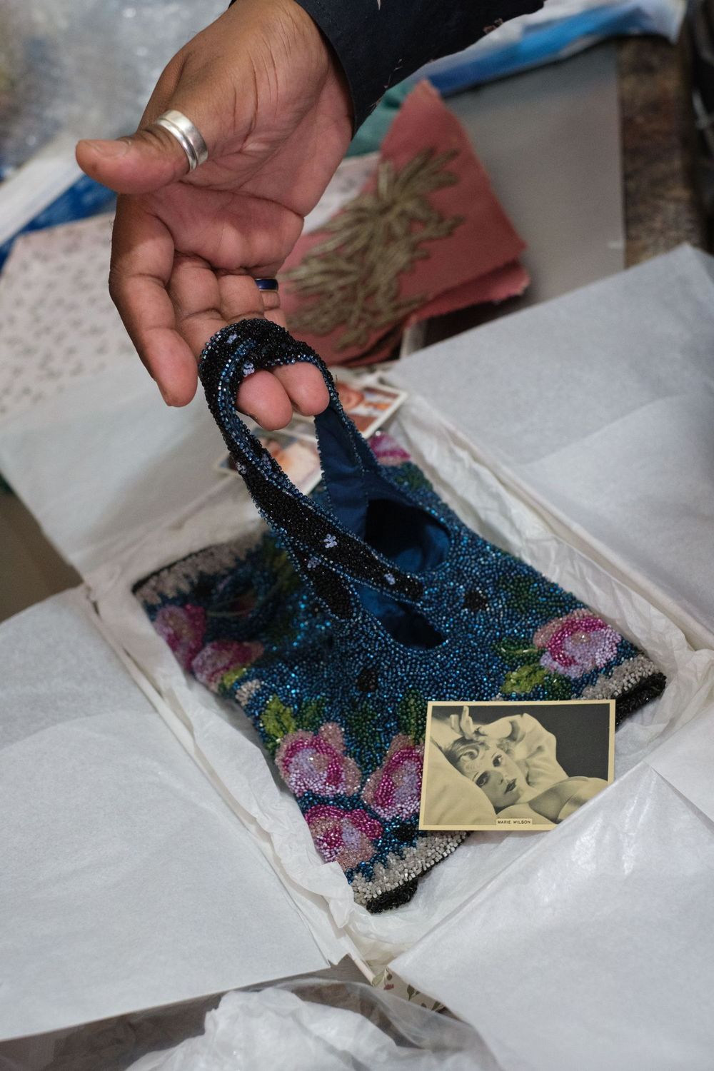 A hand holds a sparkly blue and pink sequined ornament or decorative item along with a small vintage photograph.