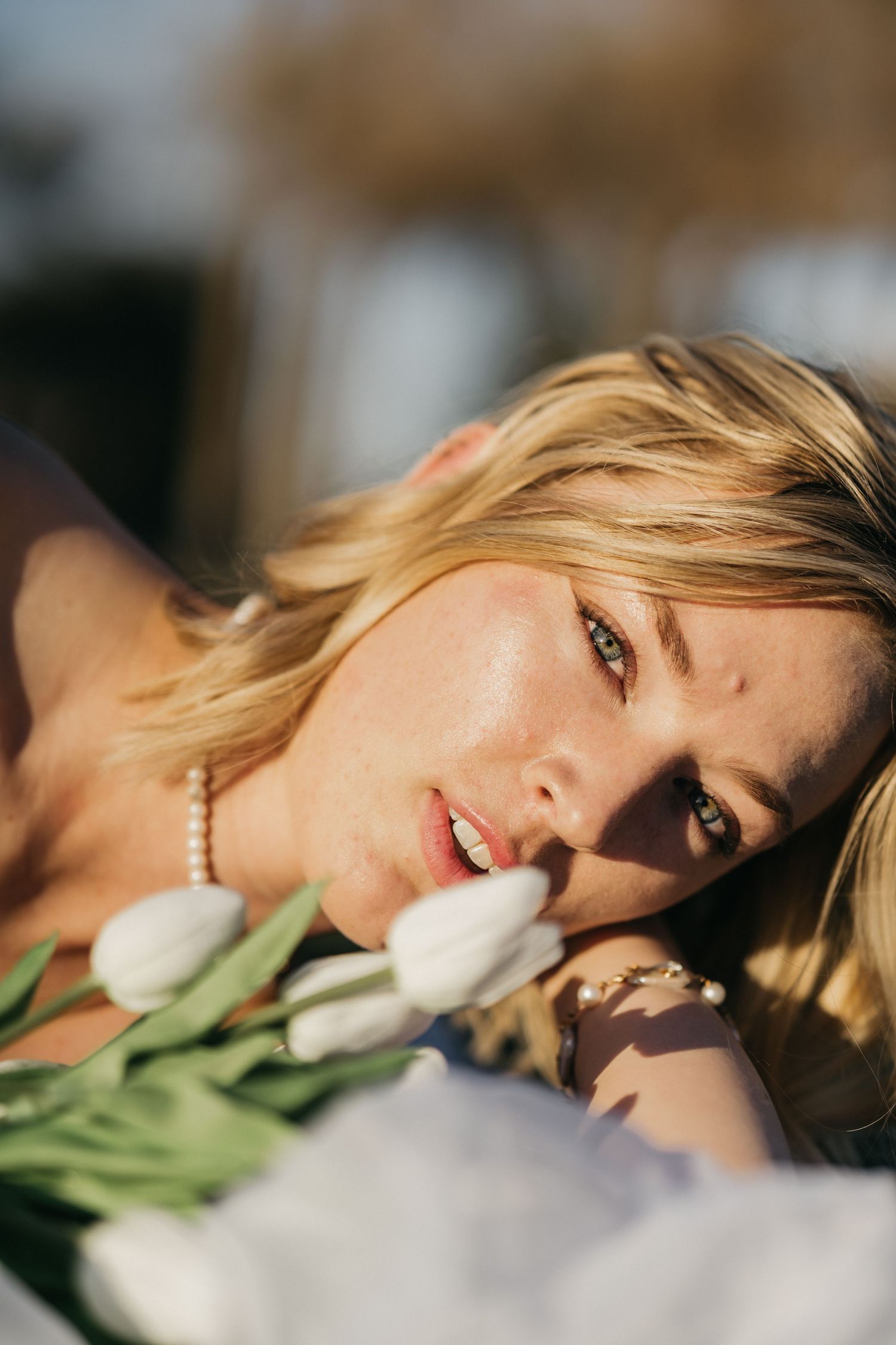 Dreamy portrait of someone resting on white bedding with fresh white tulips in warm sunlight.
