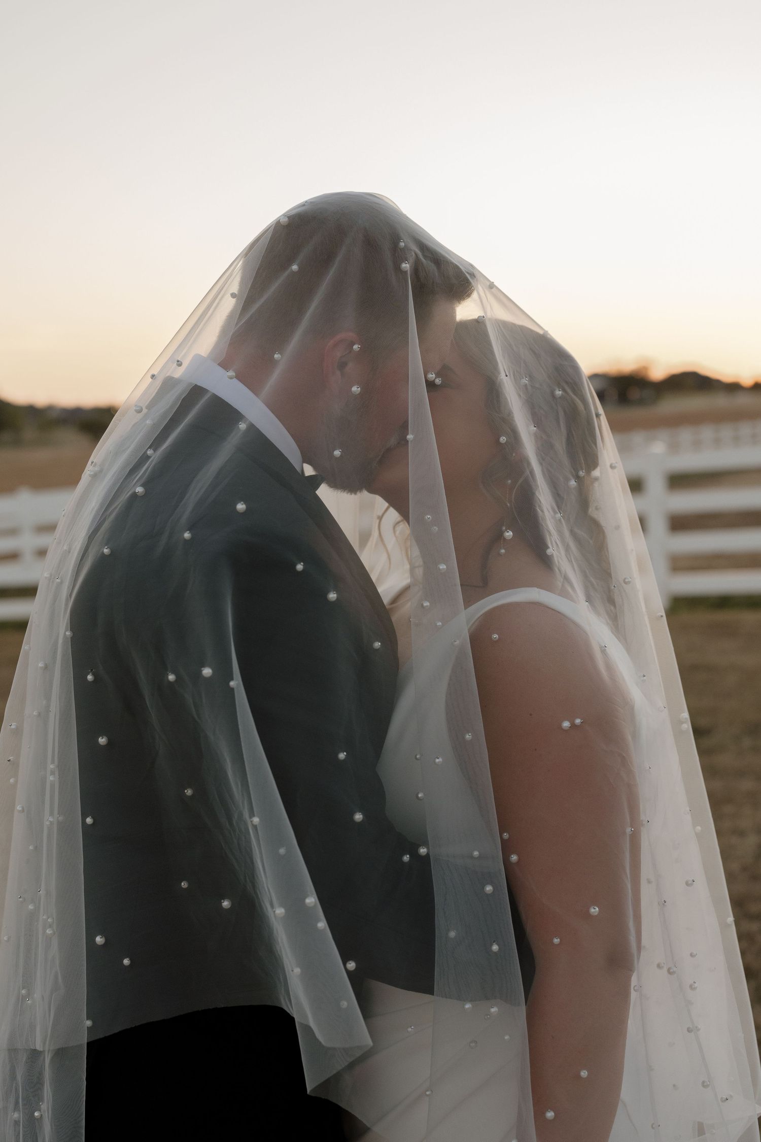 Intimate wedding moment captured under a sparkly veil during golden hour.