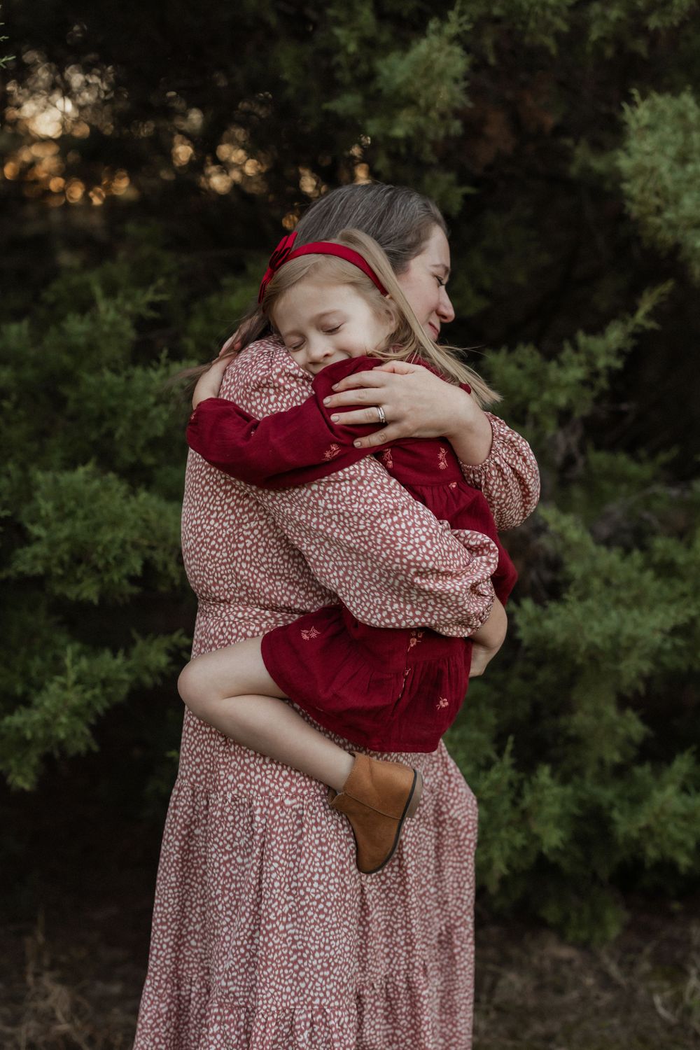 A tender embrace between two people wearing red and pink patterned clothing against a dark green forest background.