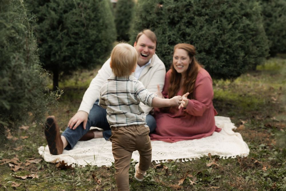 Family enjoys a playful moment on blanket at Christmas tree farm during autumn afternoon.