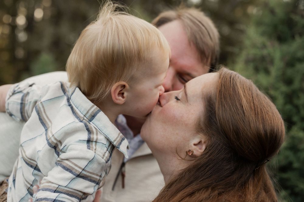 A tender family moment shared between three people embracing outdoors with greenery in the background.