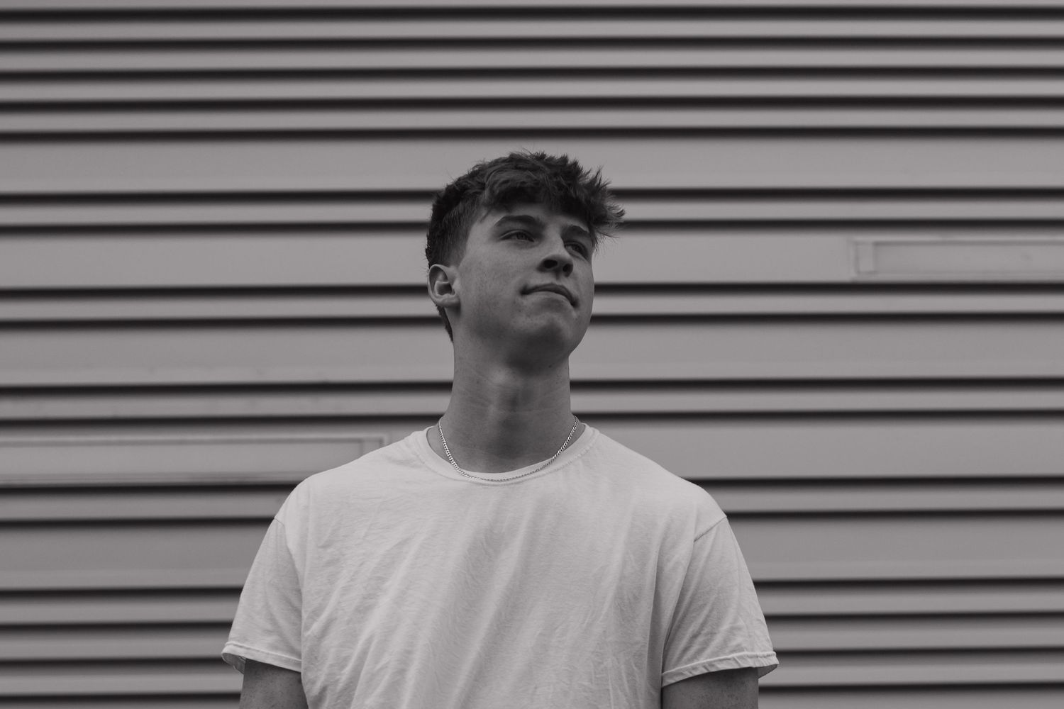 Black and white portrait against horizontal siding wearing basic white t-shirt.