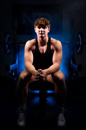 Athletic figure seated in dark gym setting with dramatic blue lighting.