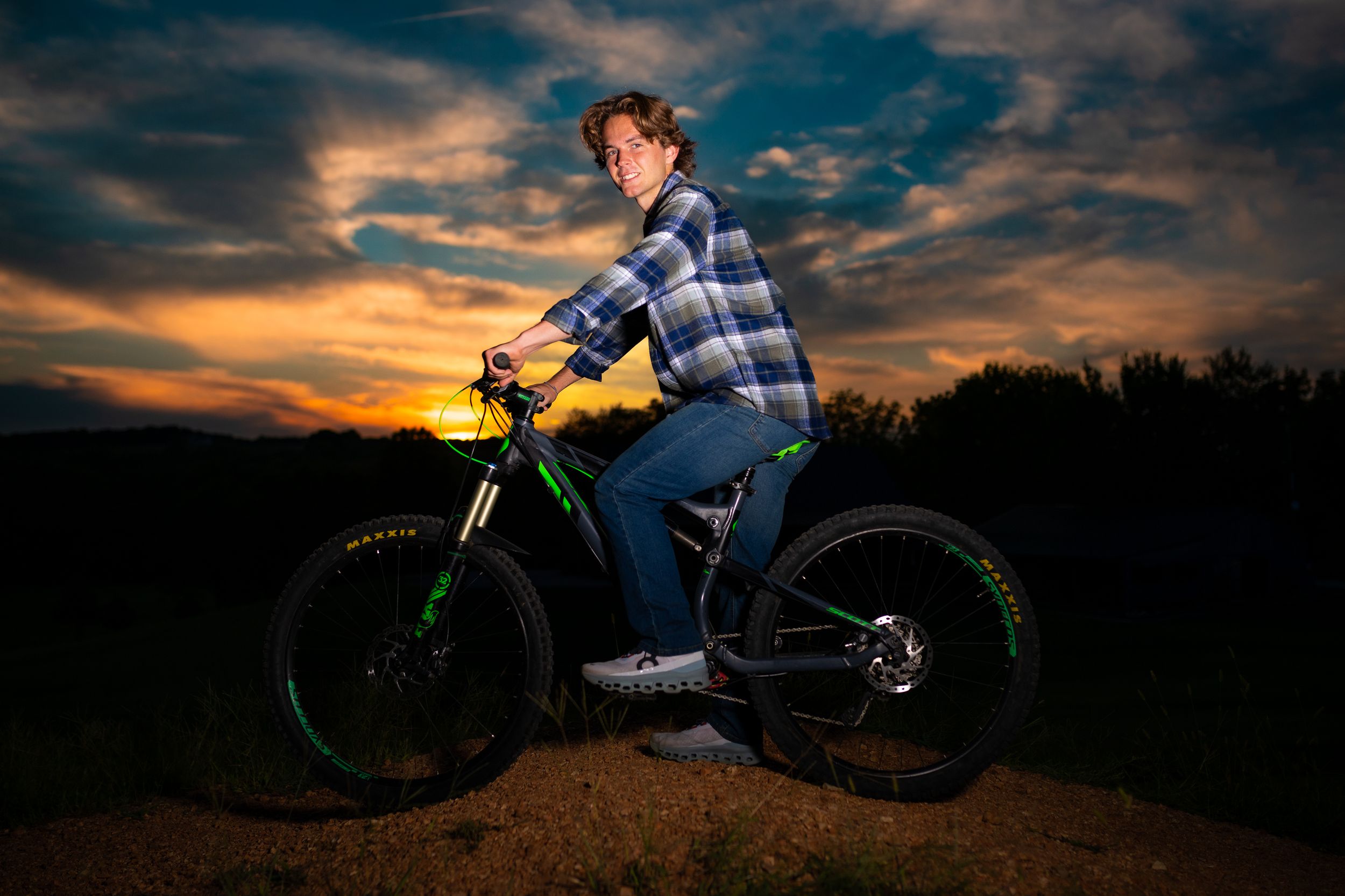 Mountain biker poses on trail against dramatic sunset sky.