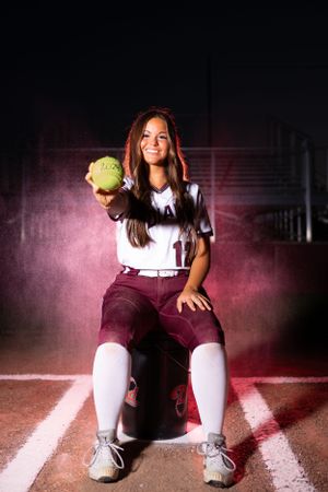 Softball player posing with yellow ball in dramatic stadium lighting.