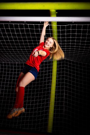 Soccer player in red uniform hanging from crossbar of the goal.
