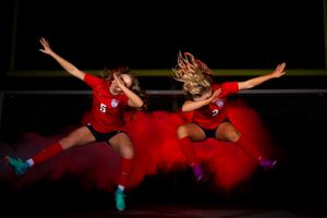 Two athletes in red uniforms performing synchronized jumps with motion blur effect.