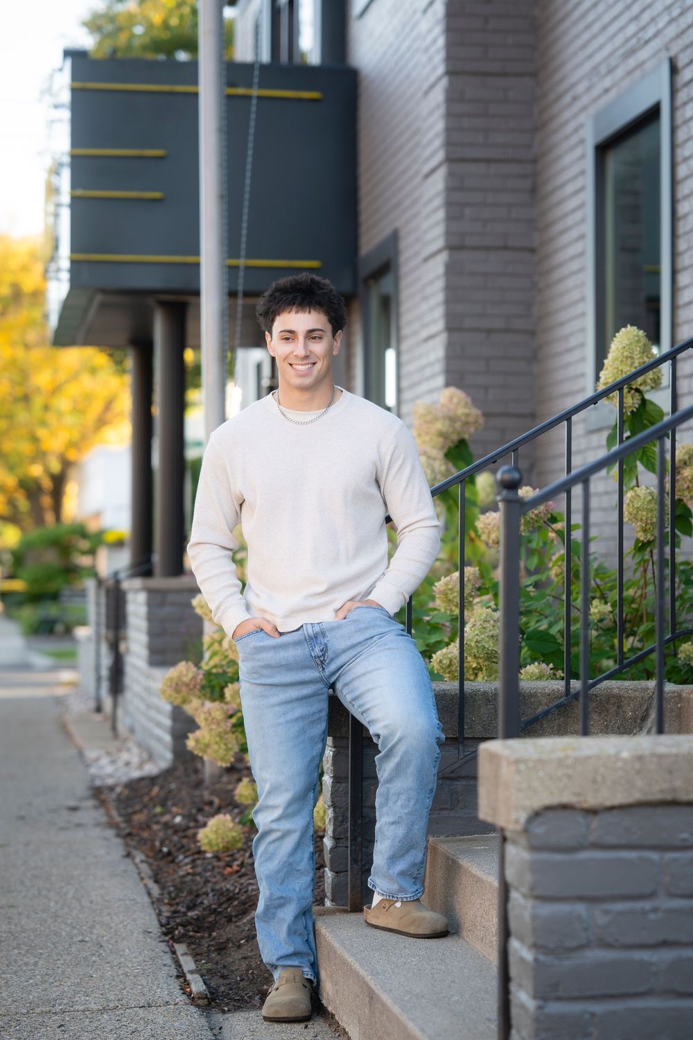 Casual portrait on stone steps with light brick building and autumn foliage in background.