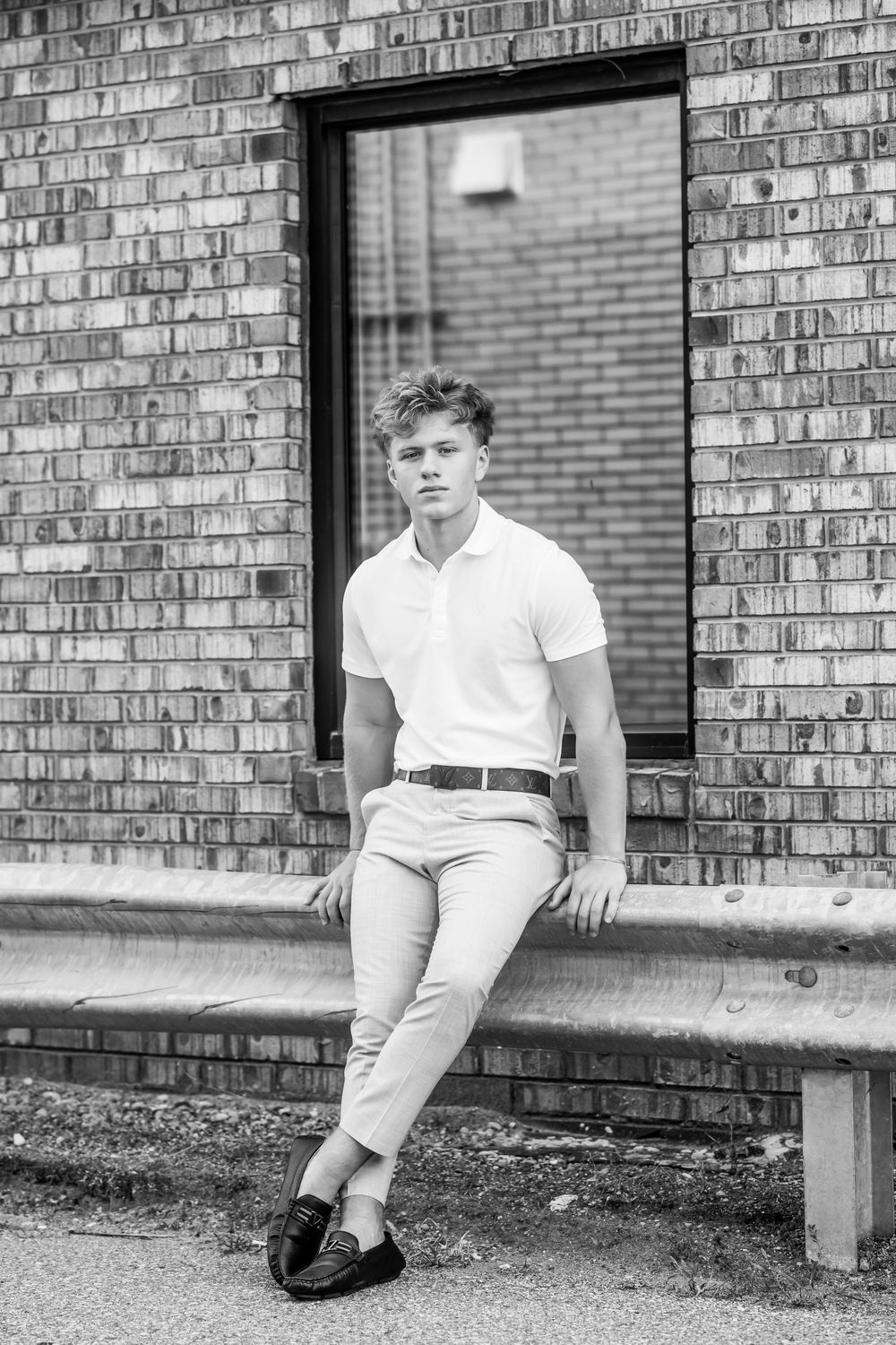 Black and white portrait of person in polo shirt seated on brick ledge.
