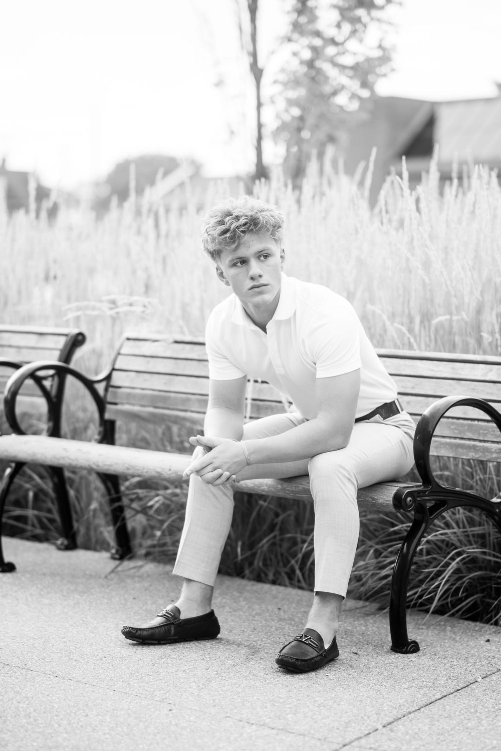 Black and white photo of person seated on park bench surrounded by tall grass.