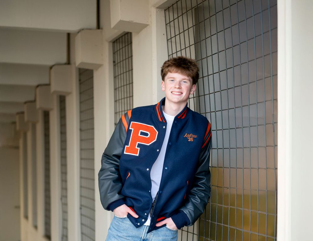 Student wearing varsity letterman jacket with P letter stands in school hallway.