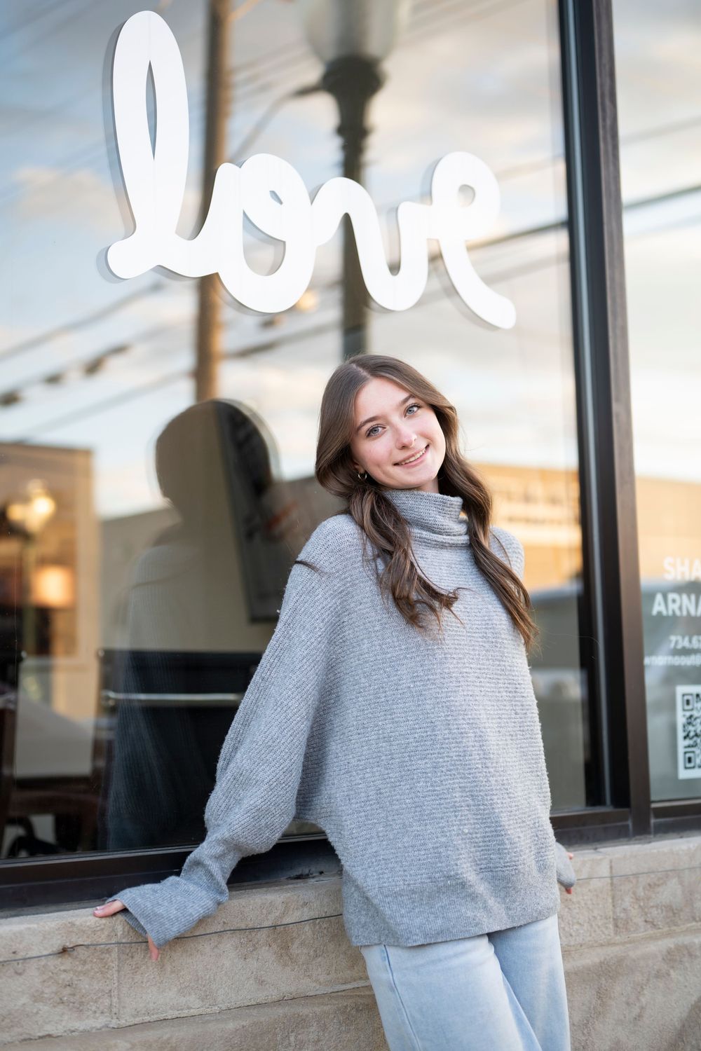 Gray sweater portrait against storefront window with white lettering.