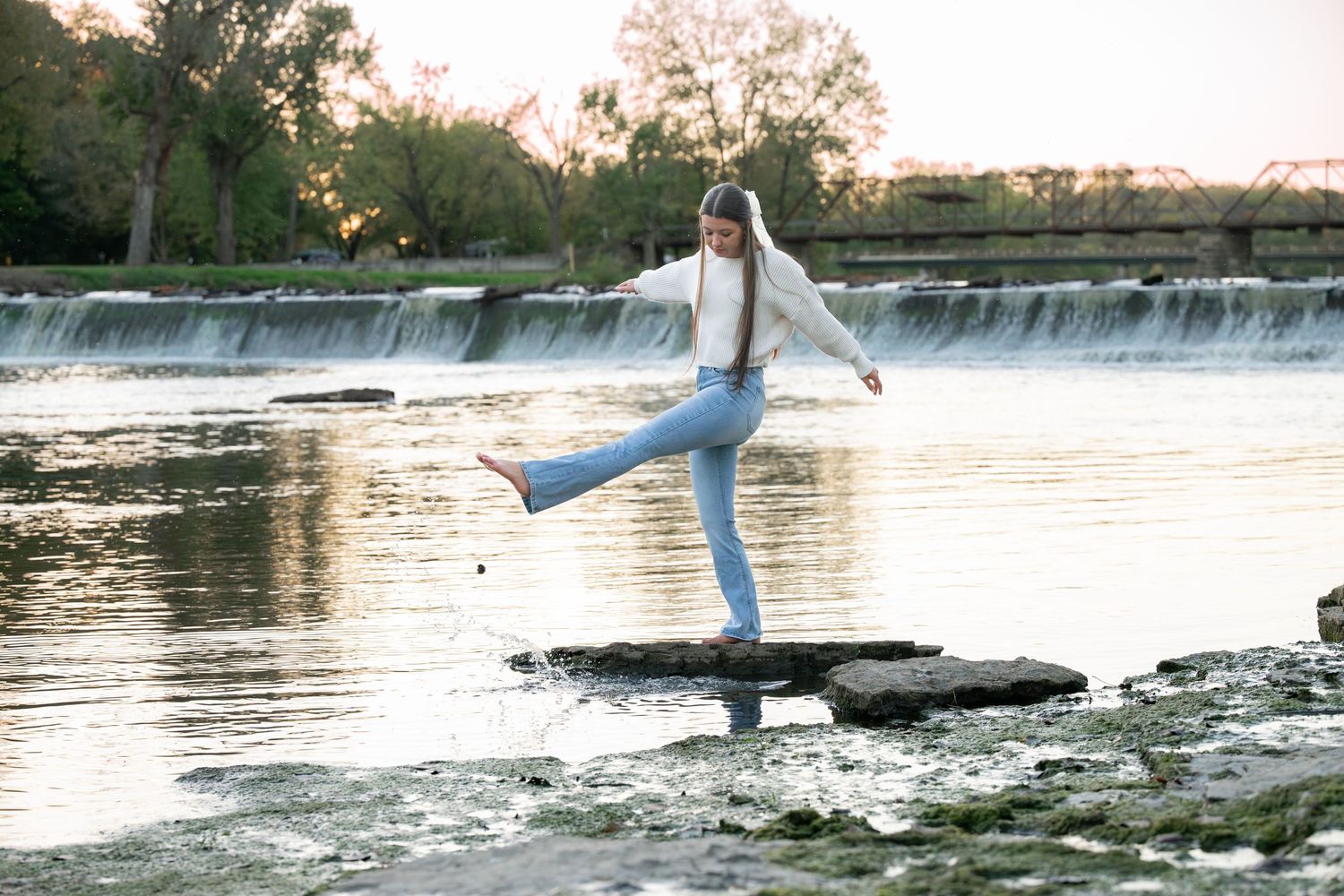 Figure strikes graceful pose on rock with waterfall backdrop during golden hour.