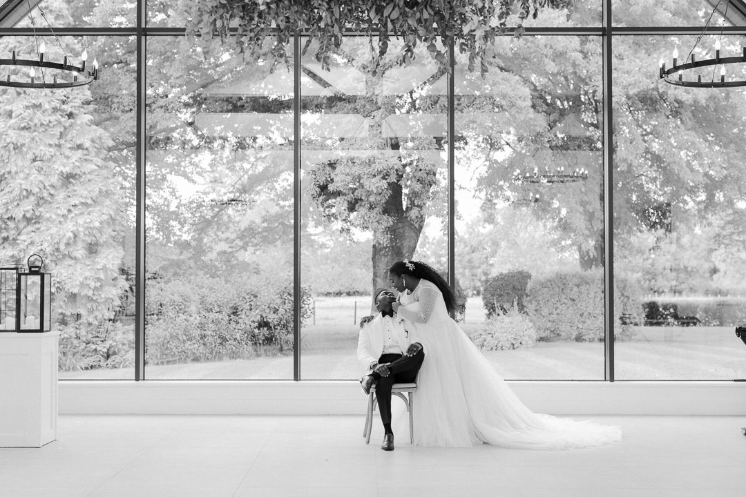Black and white wedding photo of couple dancing in front of large windows with scenic backdrop.