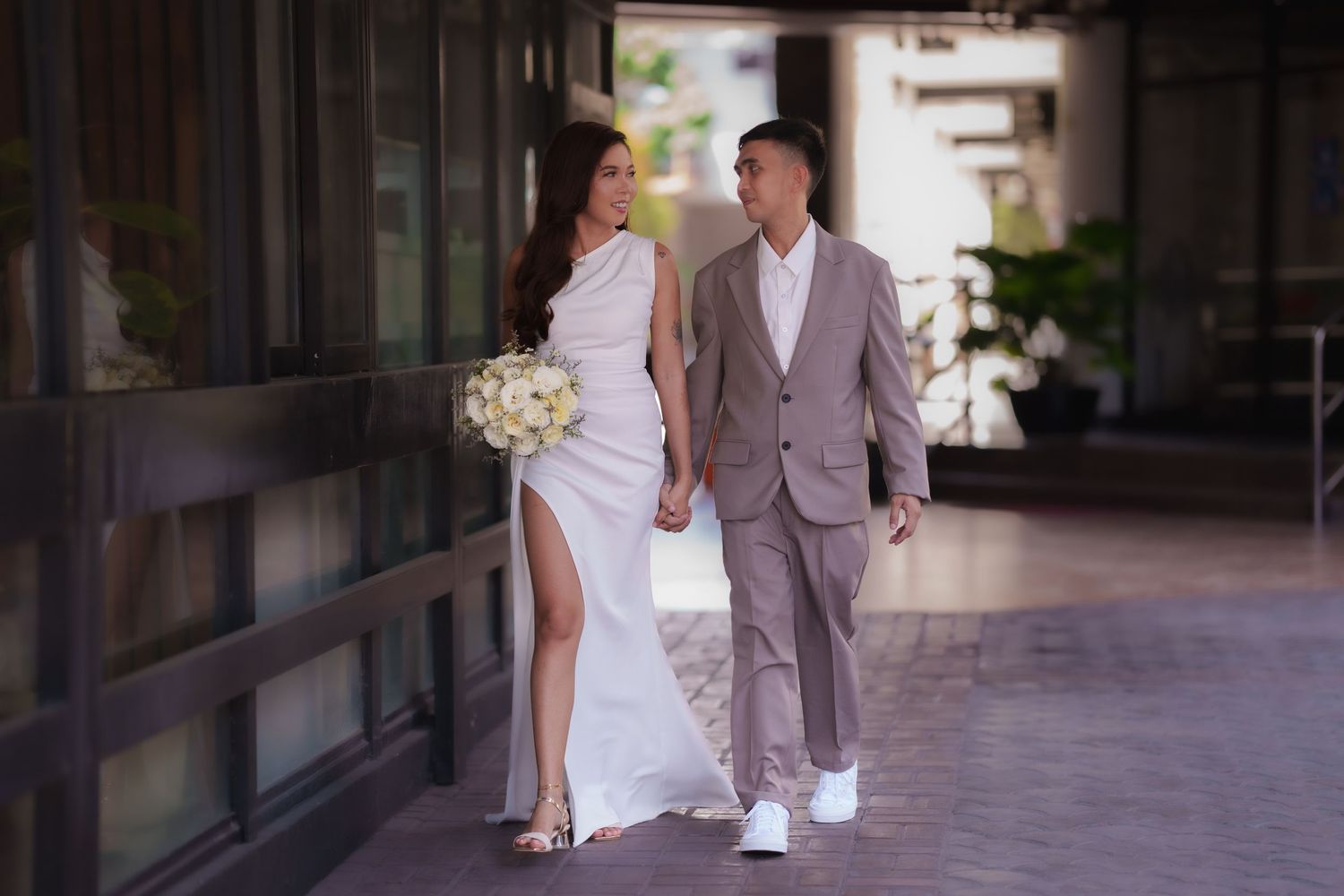 Wedding party walks together along a modern building exterior with glass windows.