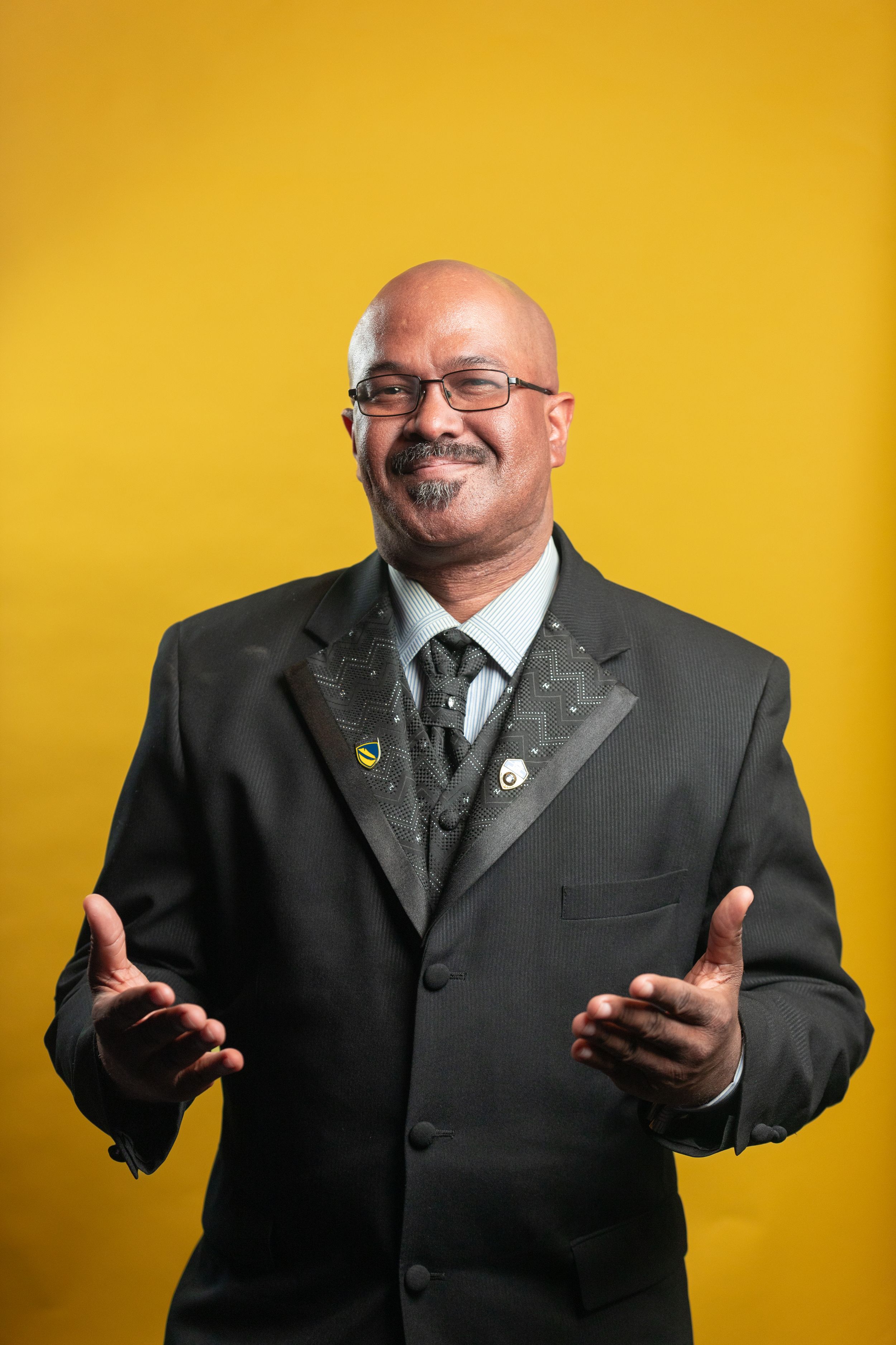 Professional portrait against yellow background showing welcoming gesture.