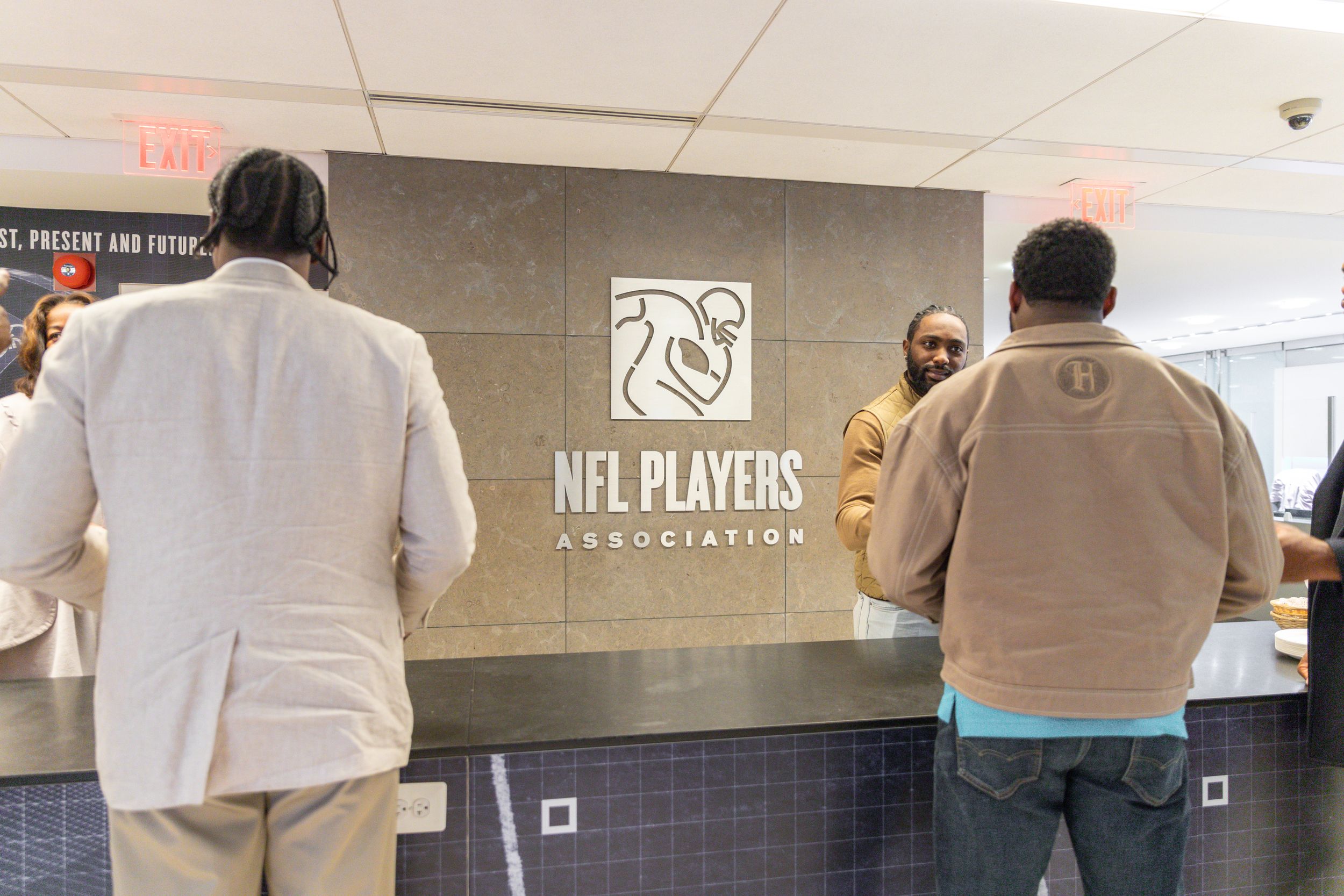 People gather in front of NFL Players Association logo sign in an office lobby.