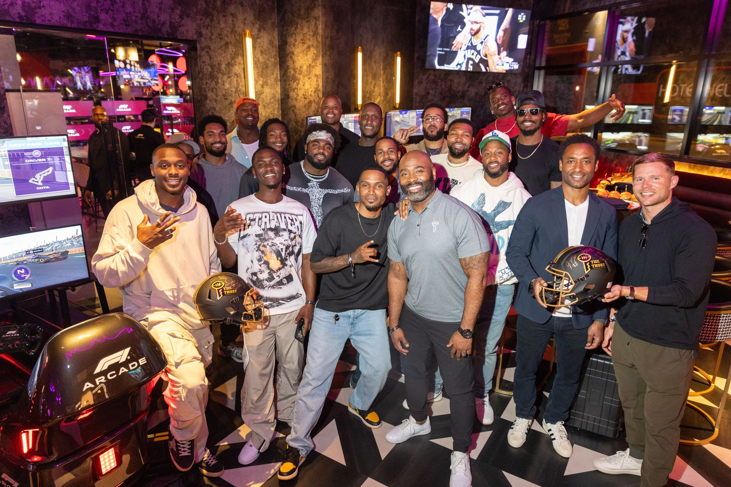 Group of people posing with gaming equipment in entertainment venue with multiple screens.