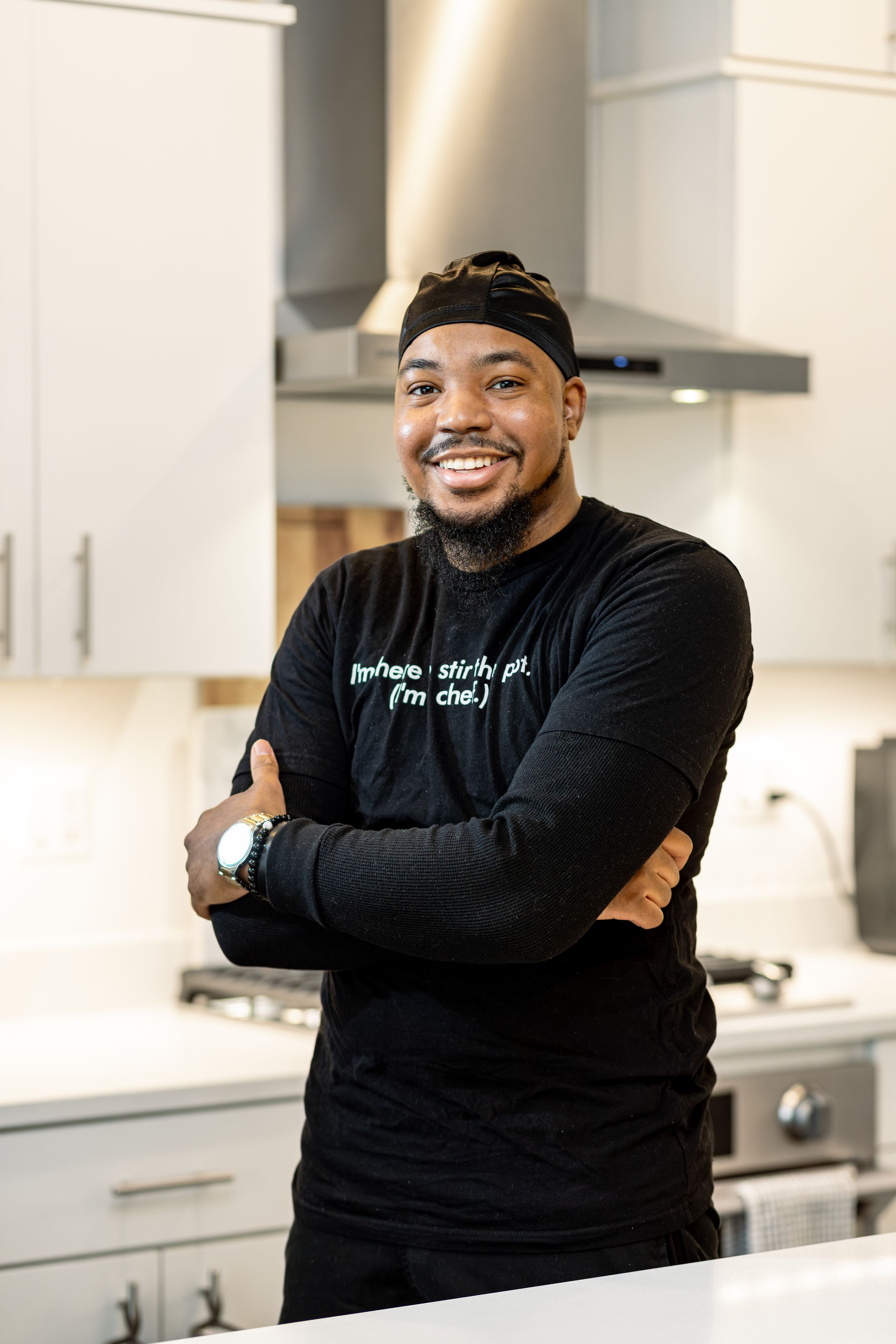 Chef wearing black uniform and headband stands confidently in a modern kitchen.