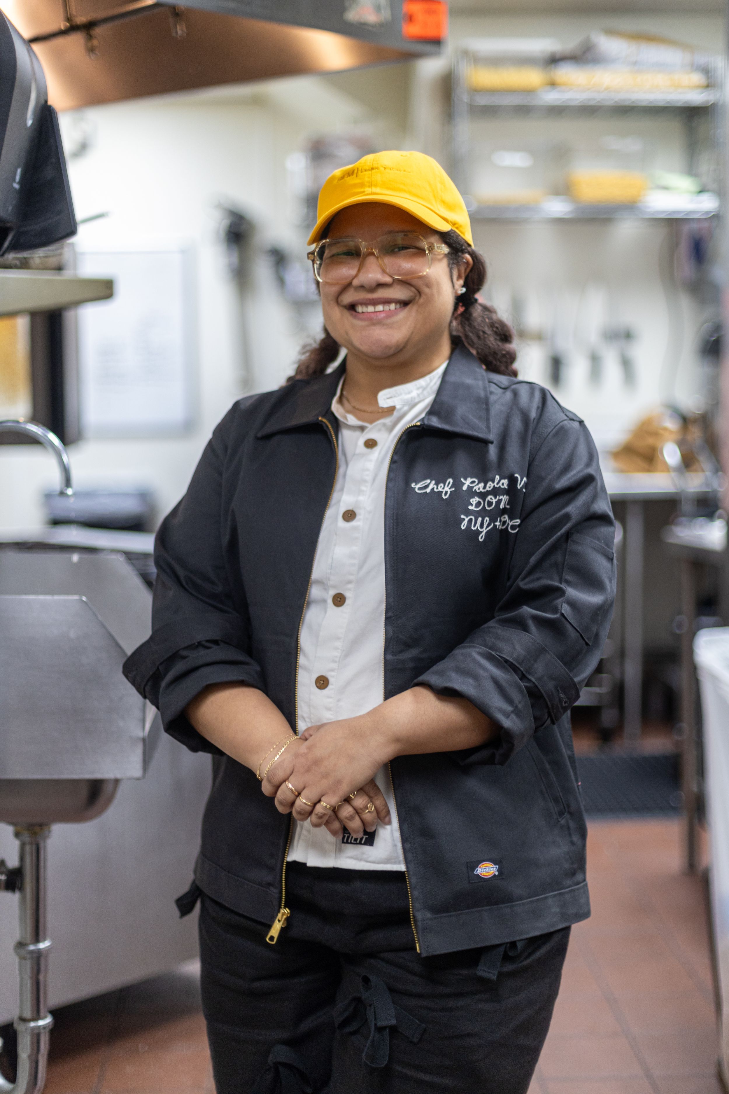 Restaurant kitchen worker in yellow cap and black uniform smiling while working.