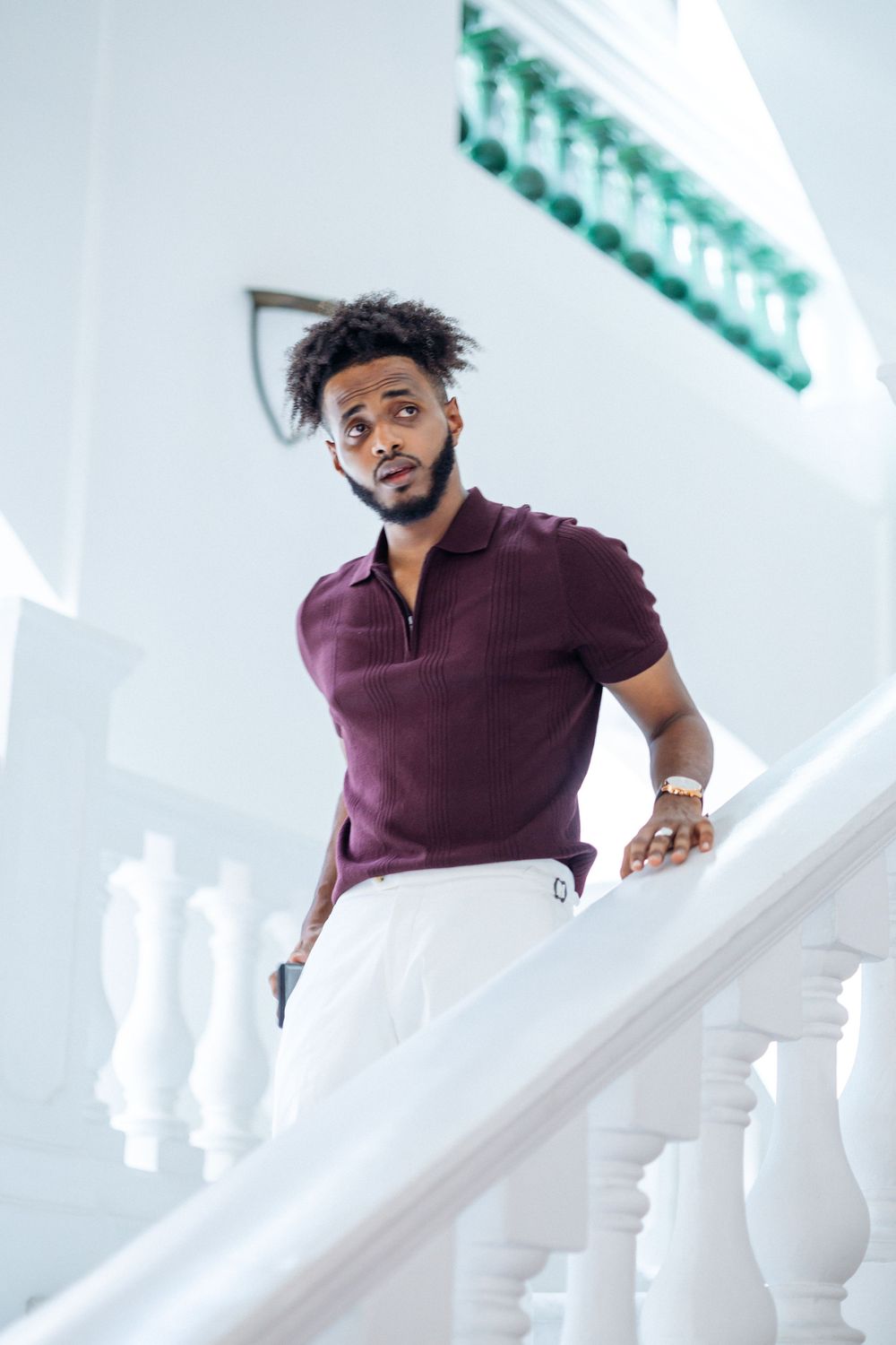 Man wearing burgundy polo shirt poses elegantly against white architectural columns in modern setting.
